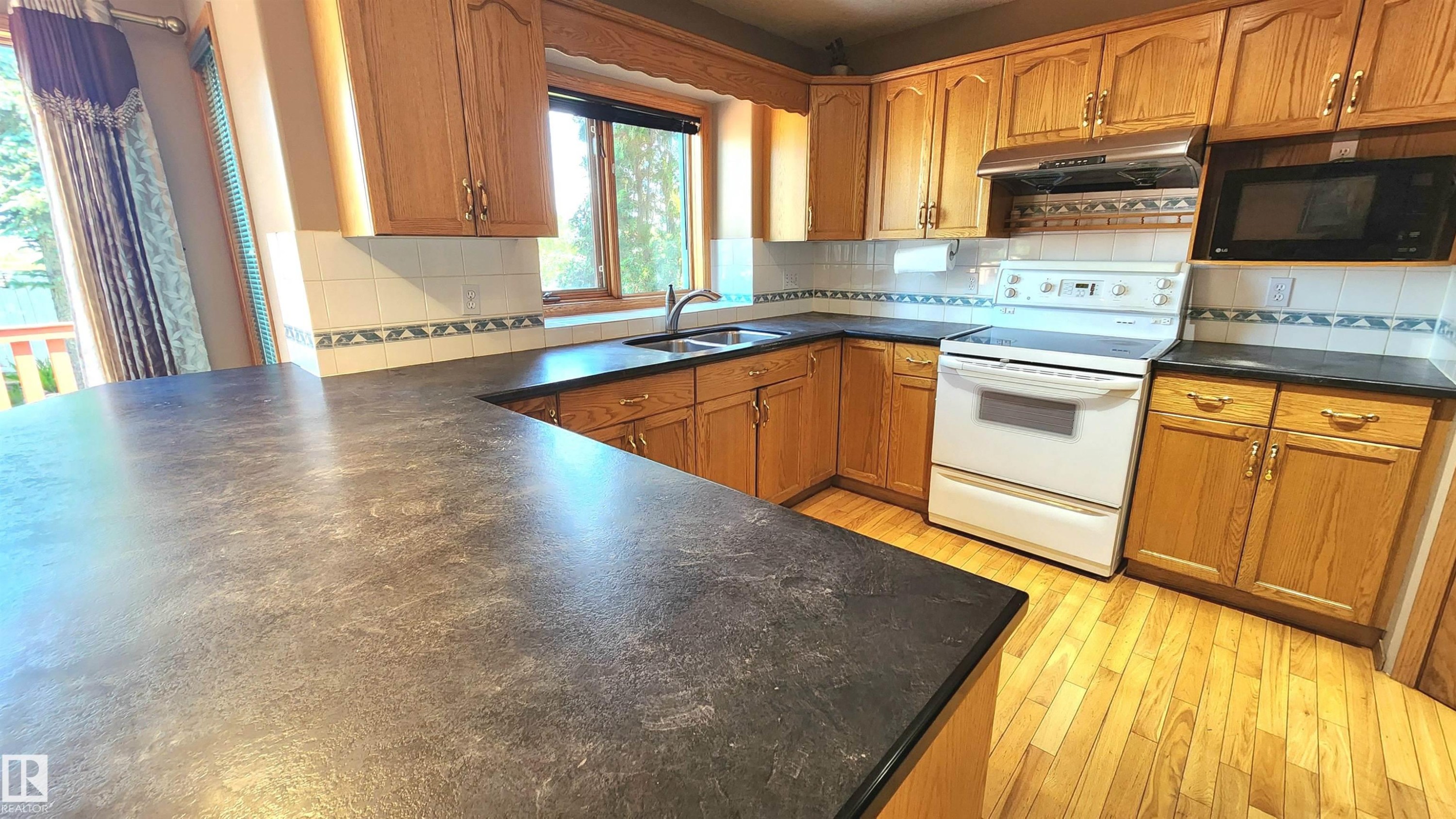 Spacious kitchen featuring extensive counter space, warm wood cabinetry, a double basin sink, and a white tile backsplash - 2708 44A Avenue, Edmonton, AB