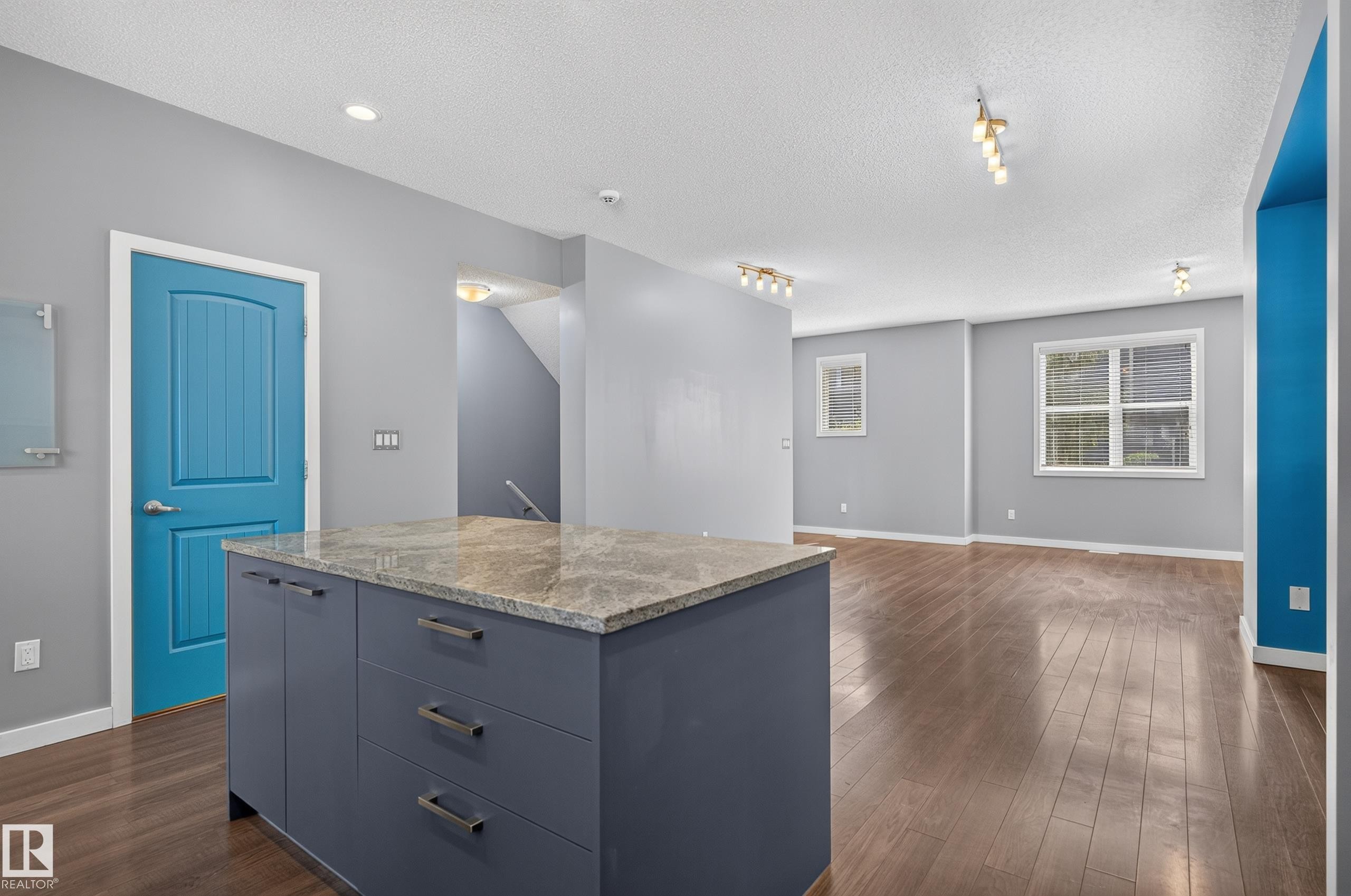 Kitchen island with a light-colored countertop and dark-toned cabinetry, set within an open-concept space featuring wood-finish flooring, recessed lighting, and track lighting fixtures - 24 655 Watt Boulevard, Edmonton, AB