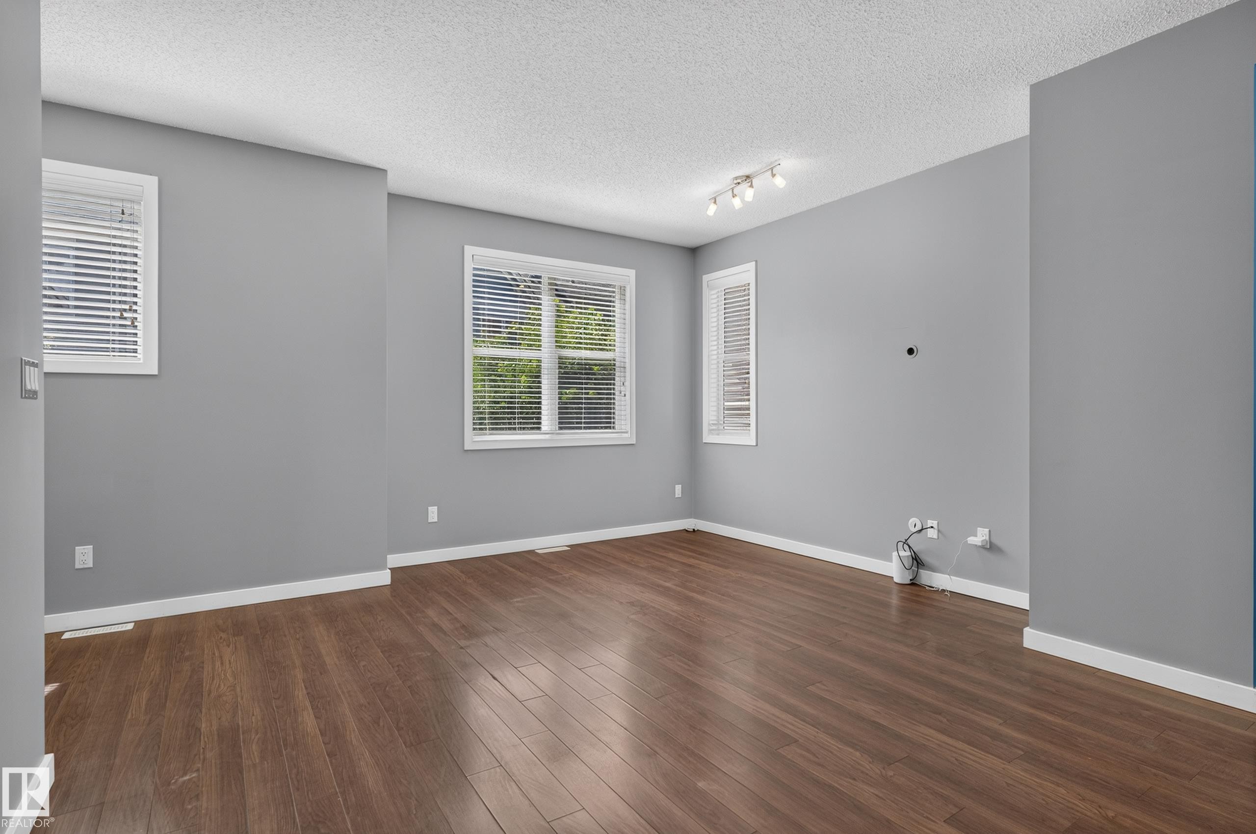 Spacious room featuring wood-finish flooring, light grey walls, white baseboards, and multiple windows with blinds - 24 655 Watt Boulevard, Edmonton, AB