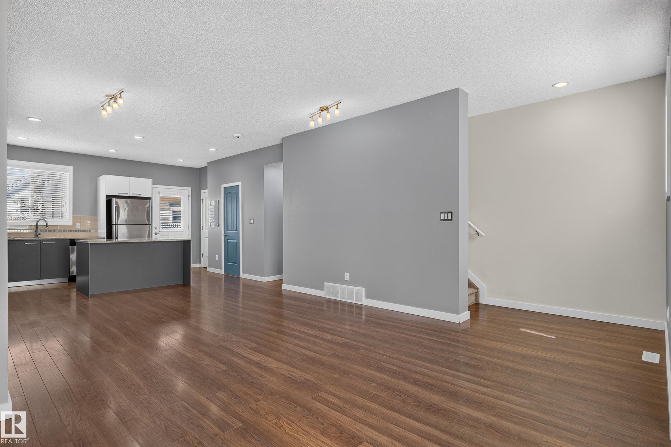 Spacious interior featuring wood-finish flooring, a kitchen island with seating, stainless steel appliances, and recessed lighting - 24 655 Watt Boulevard, Edmonton, AB