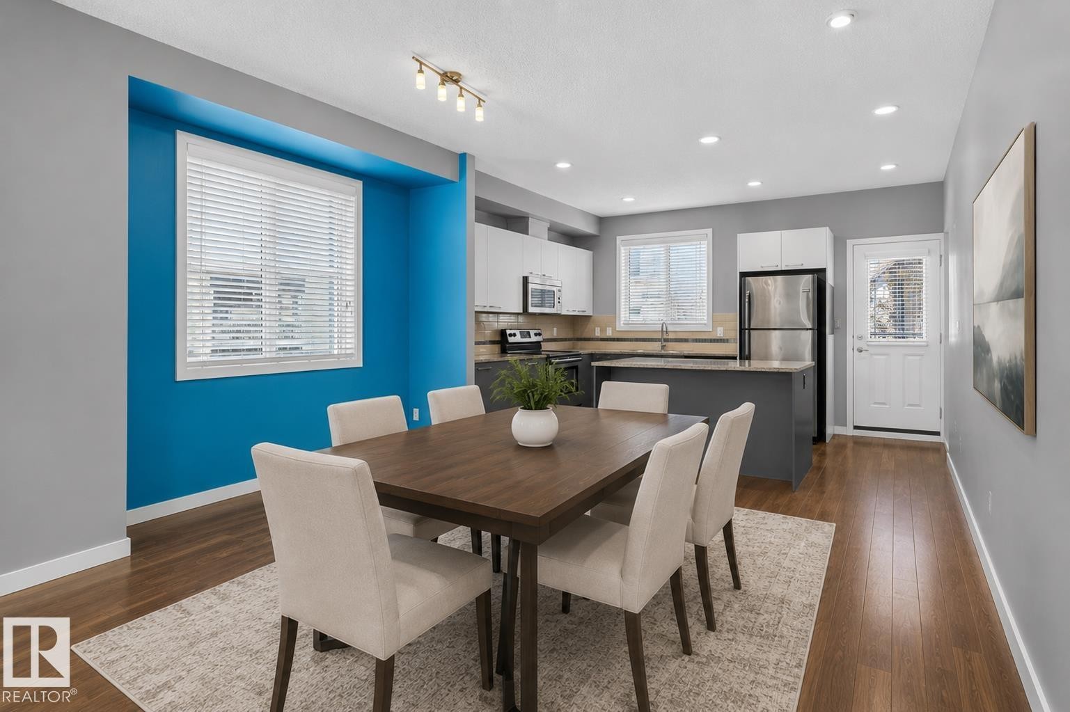 Open-concept dining and kitchen area featuring wood-finish flooring, recessed lighting, and a bright accent wall - 24 655 Watt Boulevard, Edmonton, AB