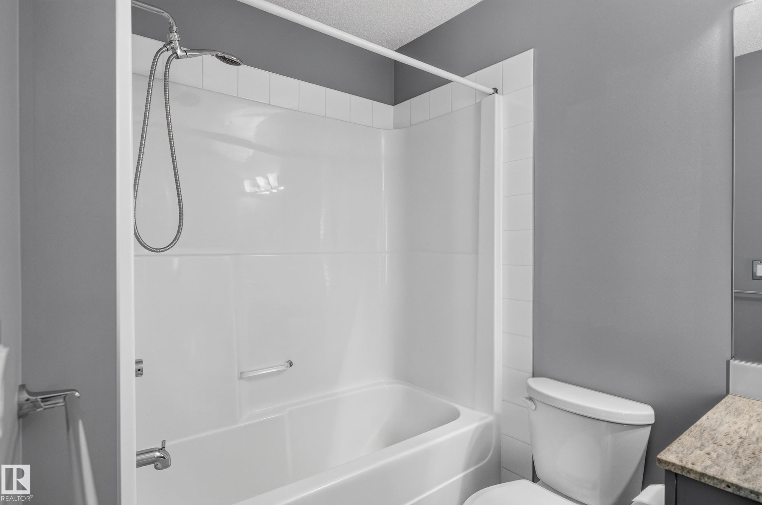 White bath and shower combination with a curved shower curtain rod, chrome fixtures, and a white toilet - 24 655 Watt Boulevard, Edmonton, AB