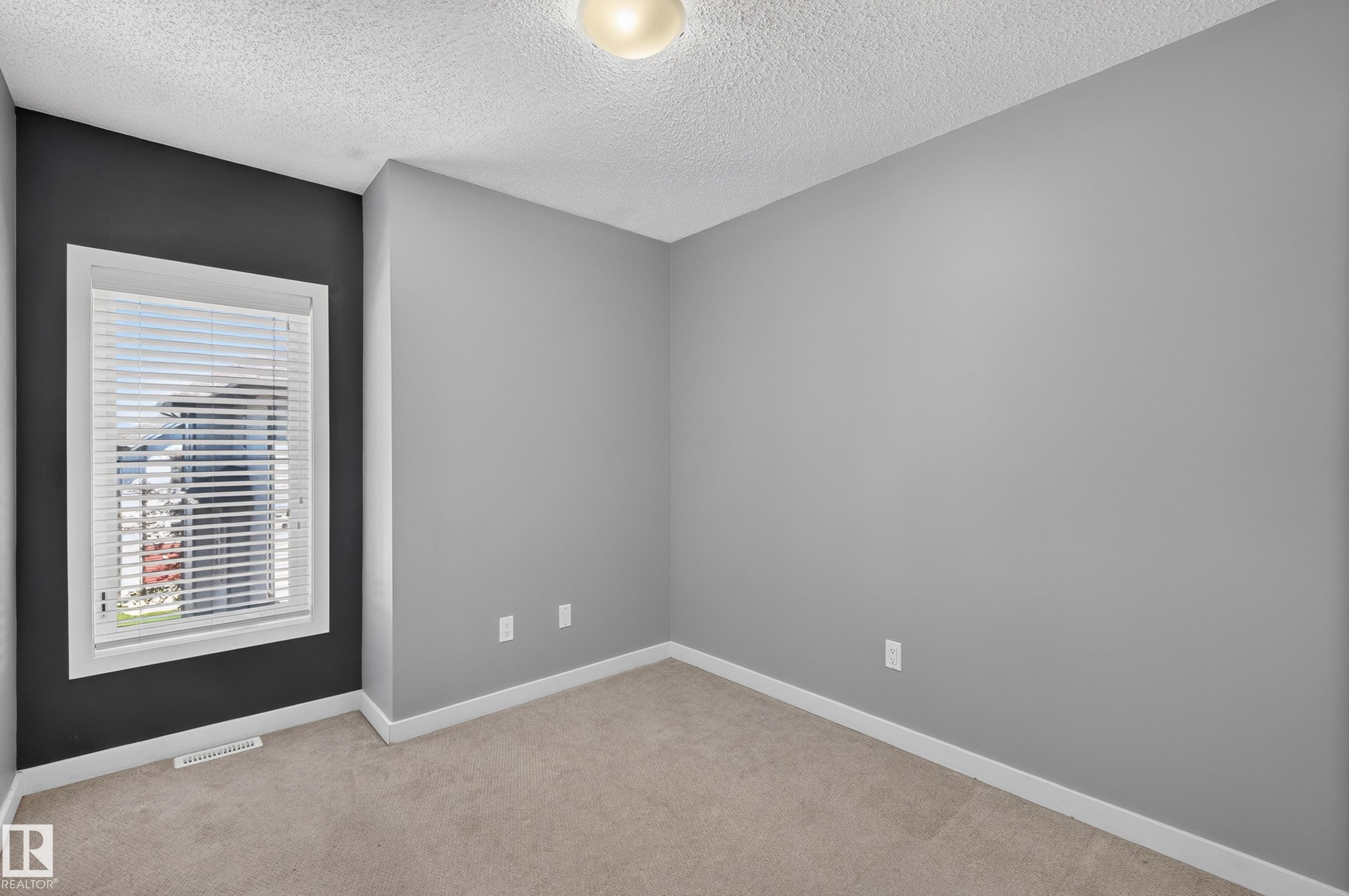 Carpeted room featuring a white-framed window with blinds, a dark accent wall, and three light gray walls - 24 655 Watt Boulevard, Edmonton, AB