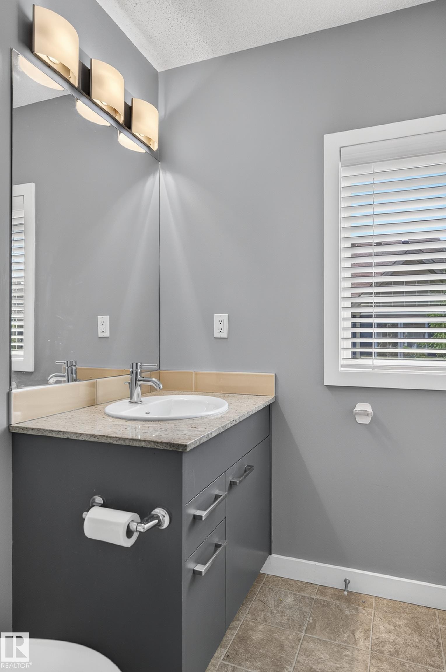 Bathroom vanity featuring a light-toned countertop, an undermount sink, and a chrome faucet - 24 655 Watt Boulevard, Edmonton, AB