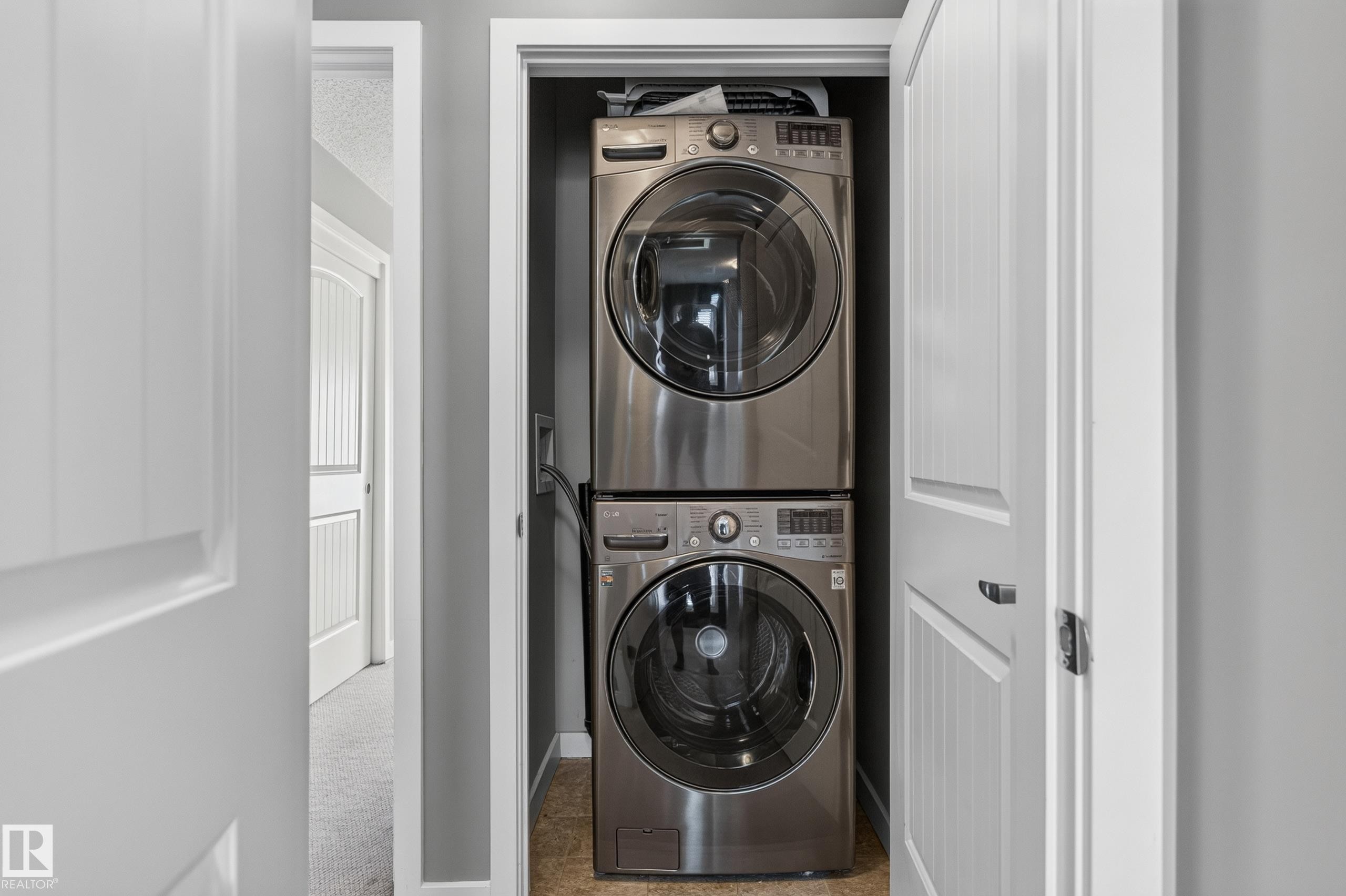 Dedicated laundry closet featuring a stacked washer and dryer, tile flooring, and white paneled doors - 24 655 Watt Boulevard, Edmonton, AB