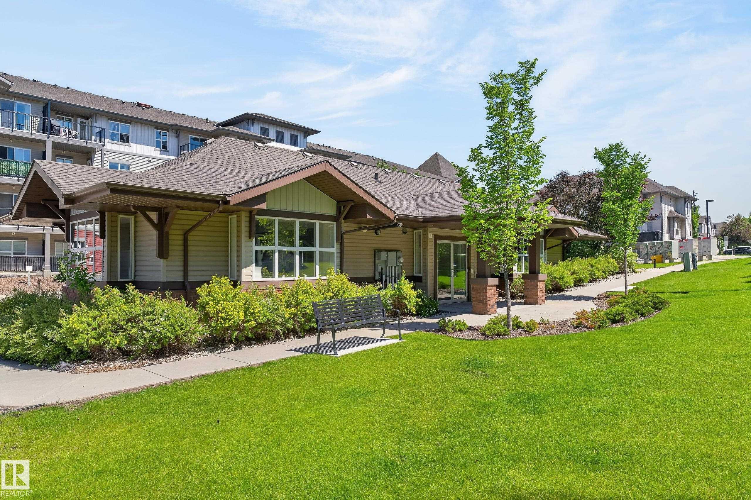 Clubhouse exterior featuring a gabled roofline, wood-finish siding, large windows, and a covered entry - 24 655 Watt Boulevard, Edmonton, AB