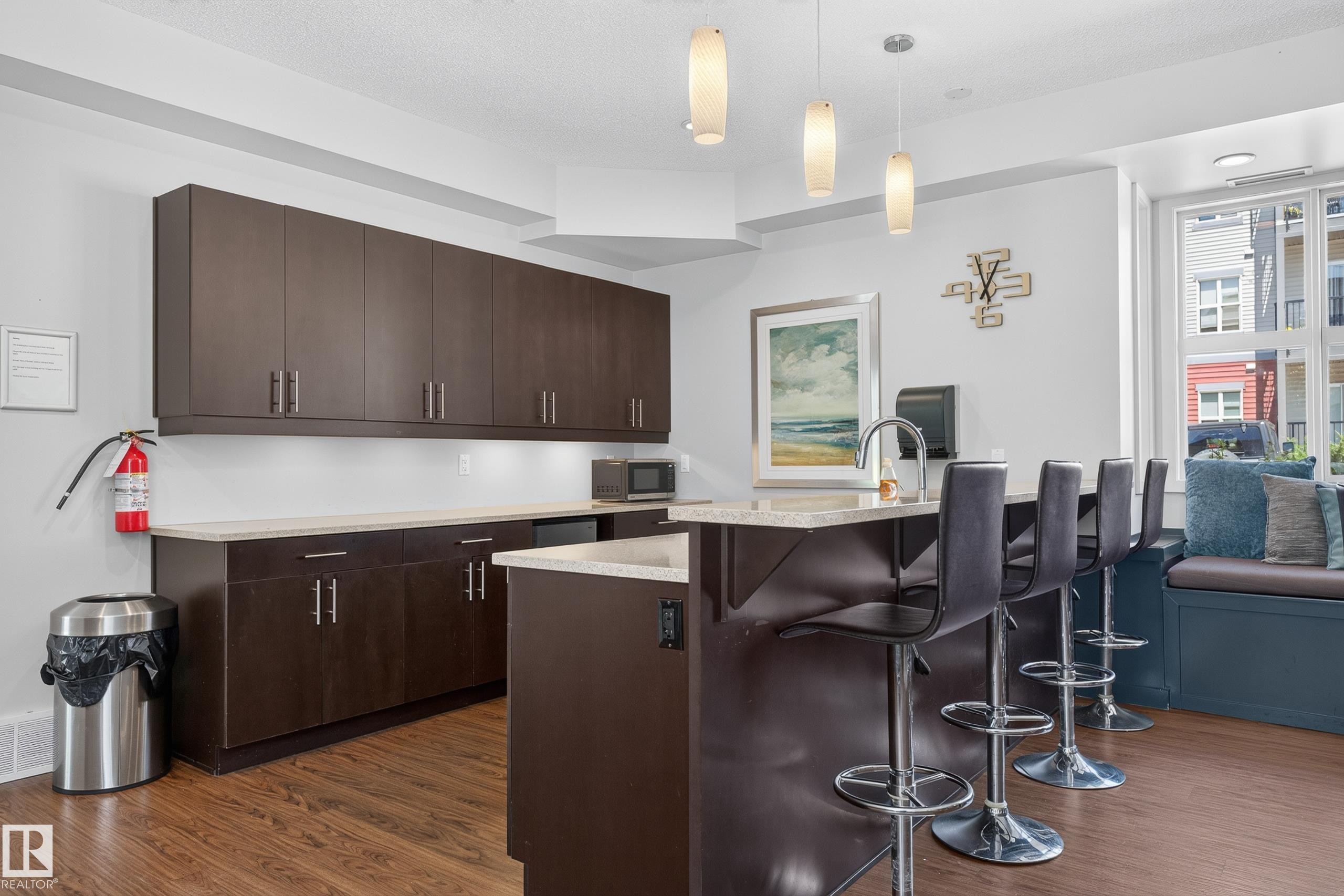 Kitchenette with extensive dark wood-finish cabinetry, light-toned countertops, and wood-finish flooring - 24 655 Watt Boulevard, Edmonton, AB