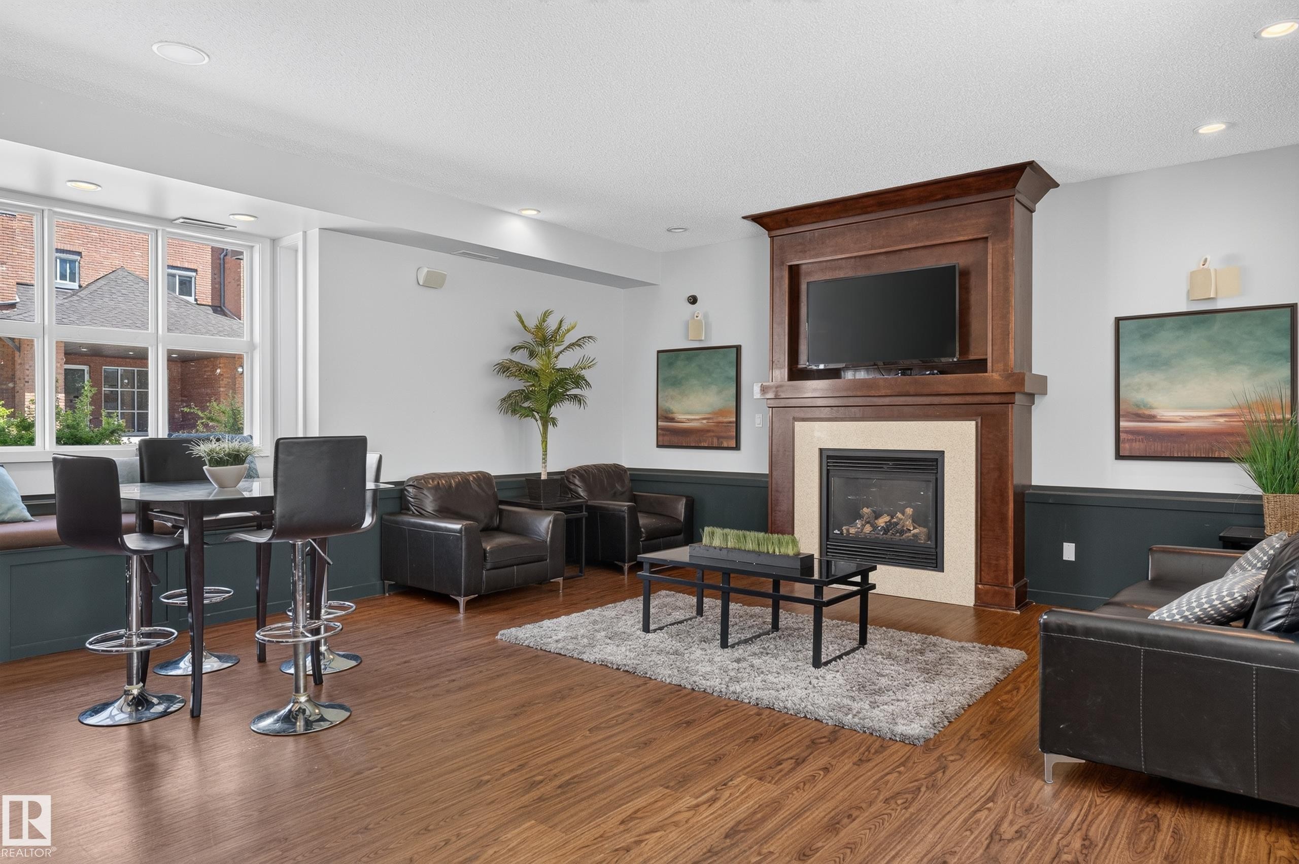 Living area featuring a rich wood-finish floor, a built-in fireplace with a light-toned surround, a prominent dark wood mantelpiece, recessed ceiling lighting, and a large multi-pane window - 24 655 Watt Boulevard, Edmonton, AB