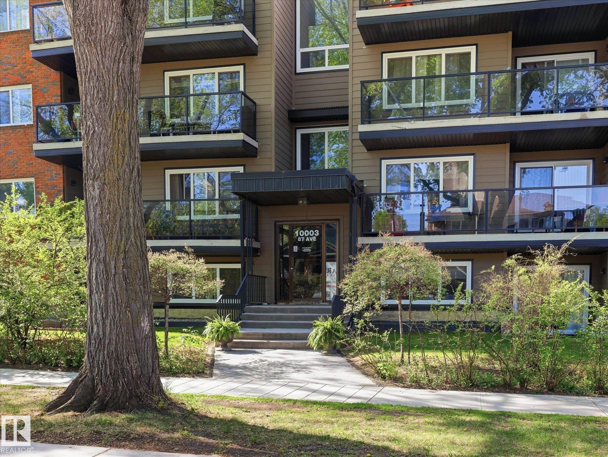 Multi-story building exterior featuring balconies with glass railings, a covered main entrance with steps, and ground-level landscaping - 301 10003 87 Avenue, Edmonton, AB - Outdoor With Facade
