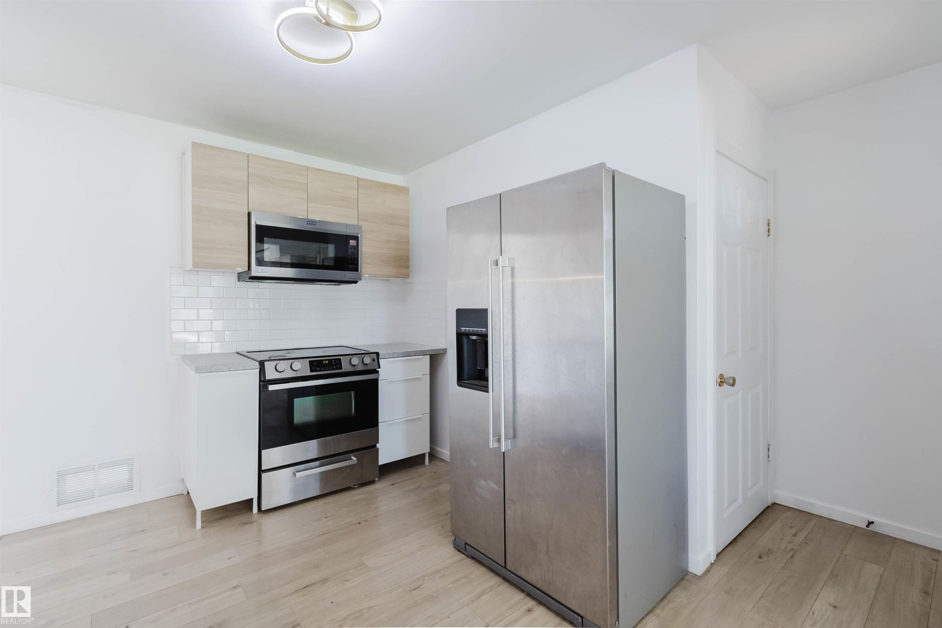 Kitchen featuring light wood-finish flooring, white subway tile backsplash, white cabinetry, and stainless steel appliances - 9606 163 Street Nw, Edmonton, AB