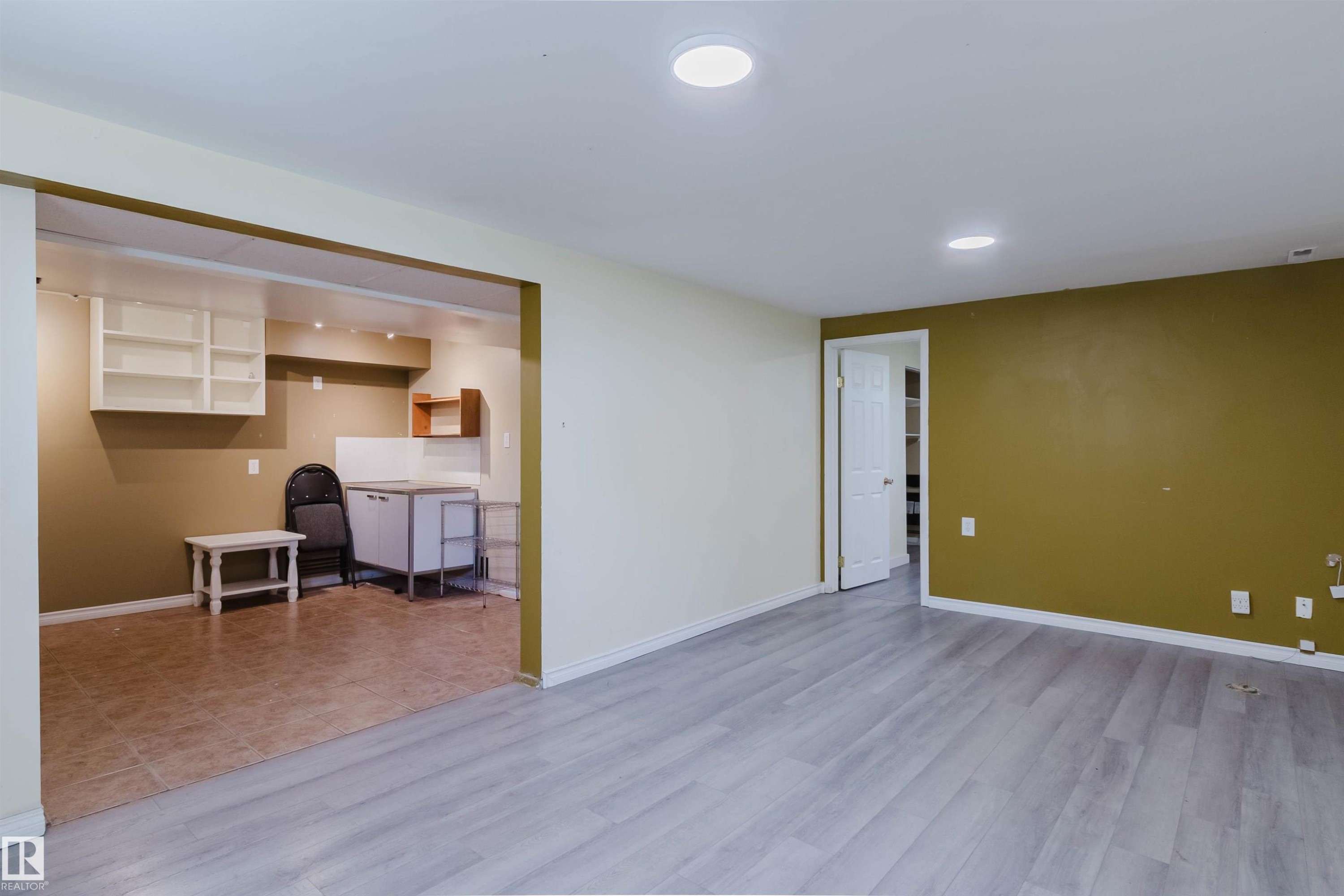Open-concept room featuring wood-finish flooring, recessed lighting, and a doorway leading to an additional space with tiled flooring and wall-mounted shelving - 9606 163 Street Nw, Edmonton, AB