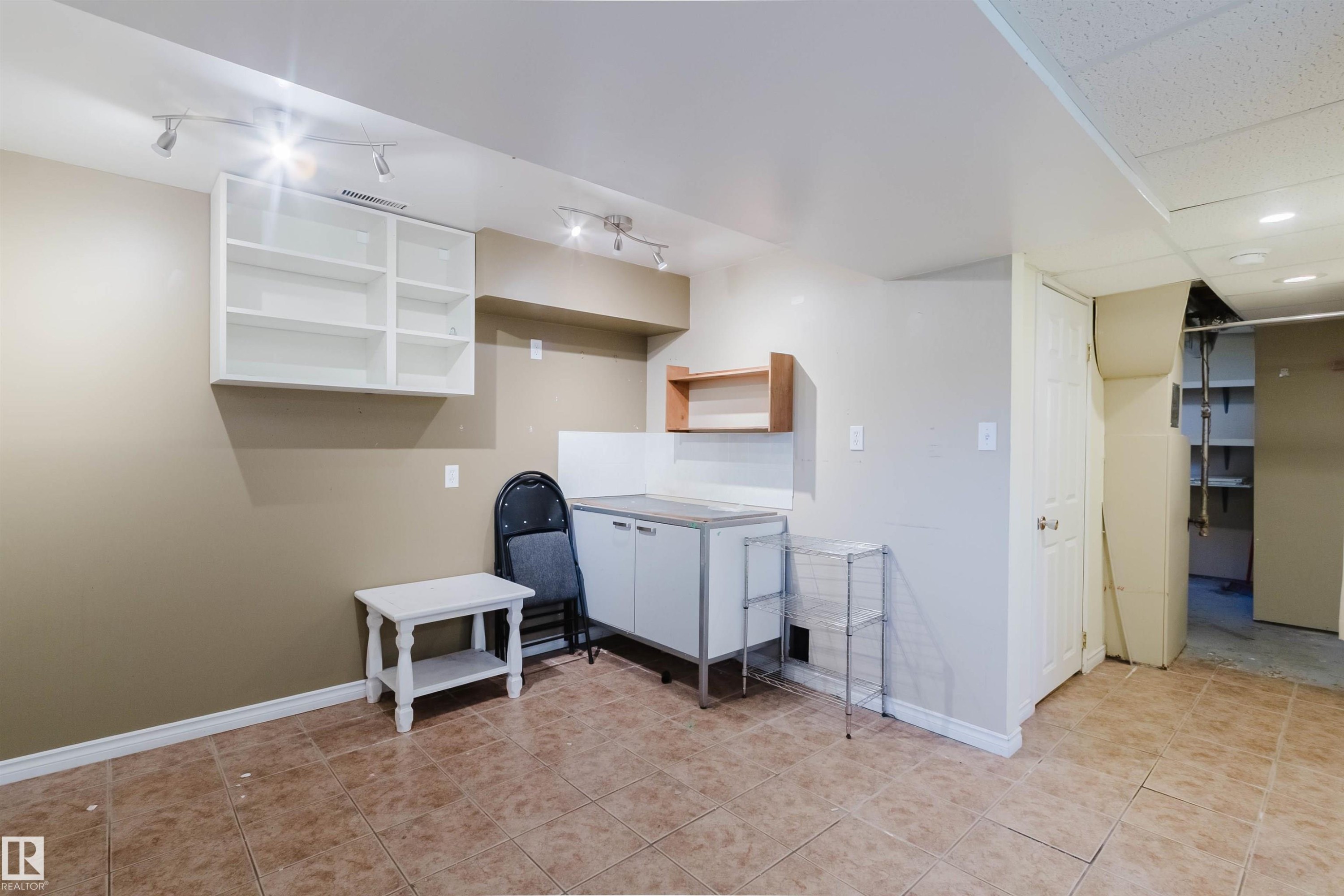 Ceramic tile flooring in an open room featuring track lighting, wall-mounted white cabinetry, a built-in sink cabinet, and an additional wood-finish shelf - 9606 163 Street Nw, Edmonton, AB