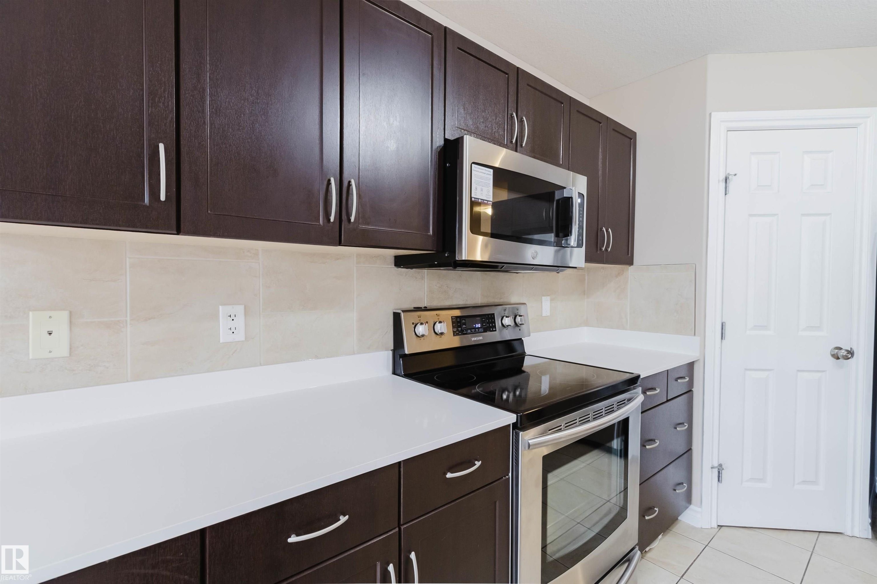 Modern kitchen featuring dark wood-finish cabinetry, bright white countertops, and a tiled backsplash - 1919 Hammond Place, Edmonton, AB