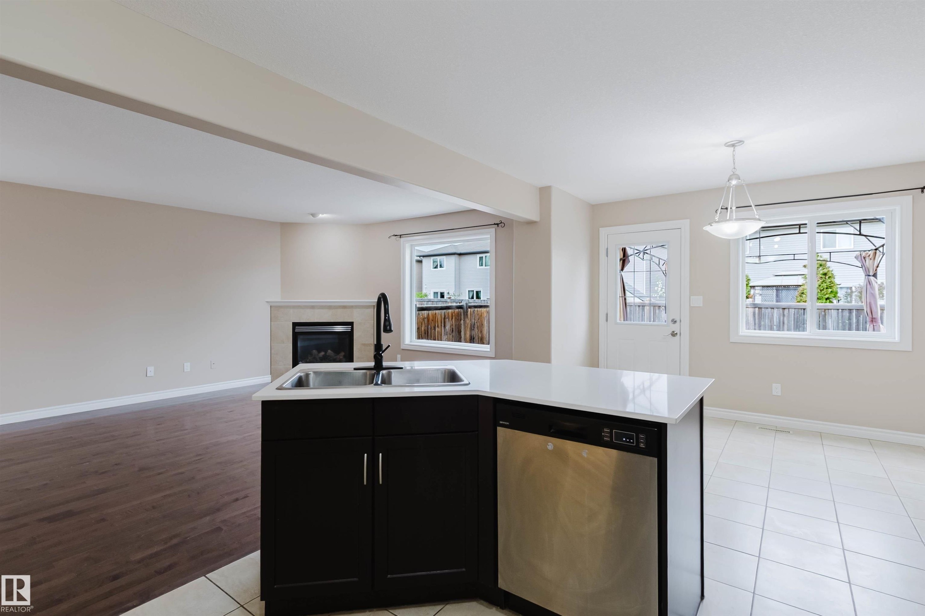 Kitchen island featuring a double-basin stainless steel sink with a matte black faucet, integrated dishwasher, dark wood-finish cabinetry, and a white countertop - 1919 Hammond Place, Edmonton, AB