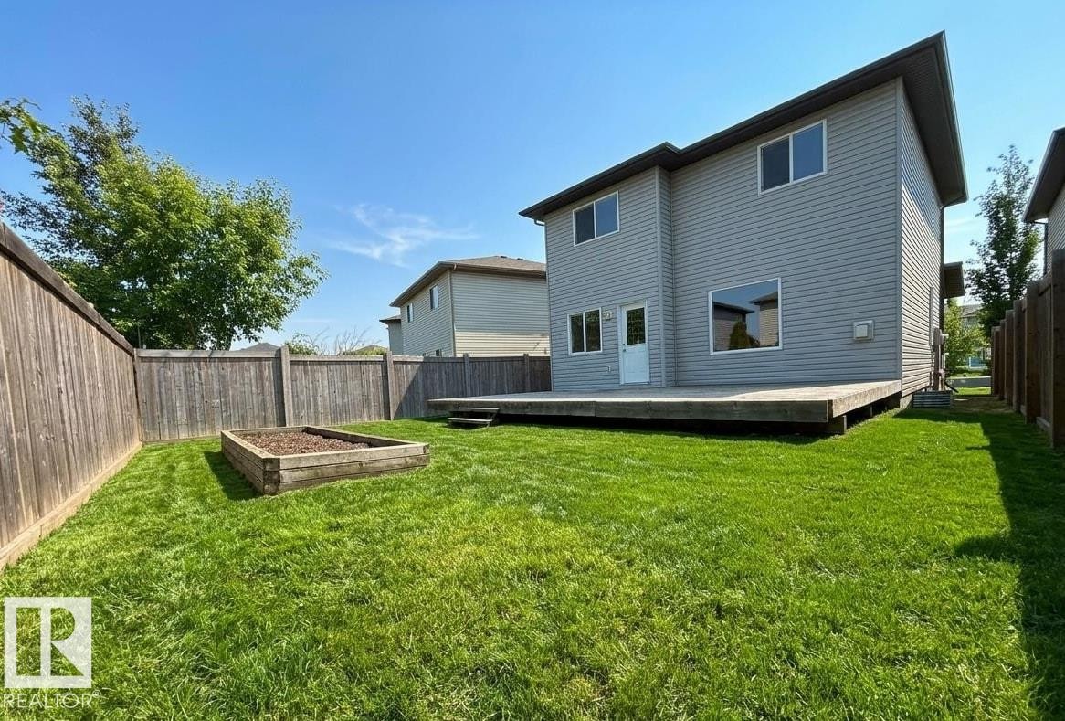 Expansive backyard featuring a large wooden deck, a raised garden bed, full privacy fencing, and a manicured lawn - 1919 Hammond Place, Edmonton, AB