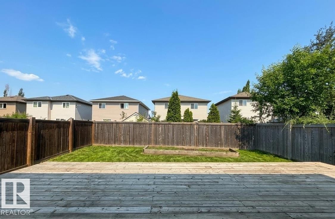 Expansive outdoor wood deck with a natural finish, bordering a fenced yard featuring a grassy area and a raised garden bed - 1919 Hammond Place, Edmonton, AB
