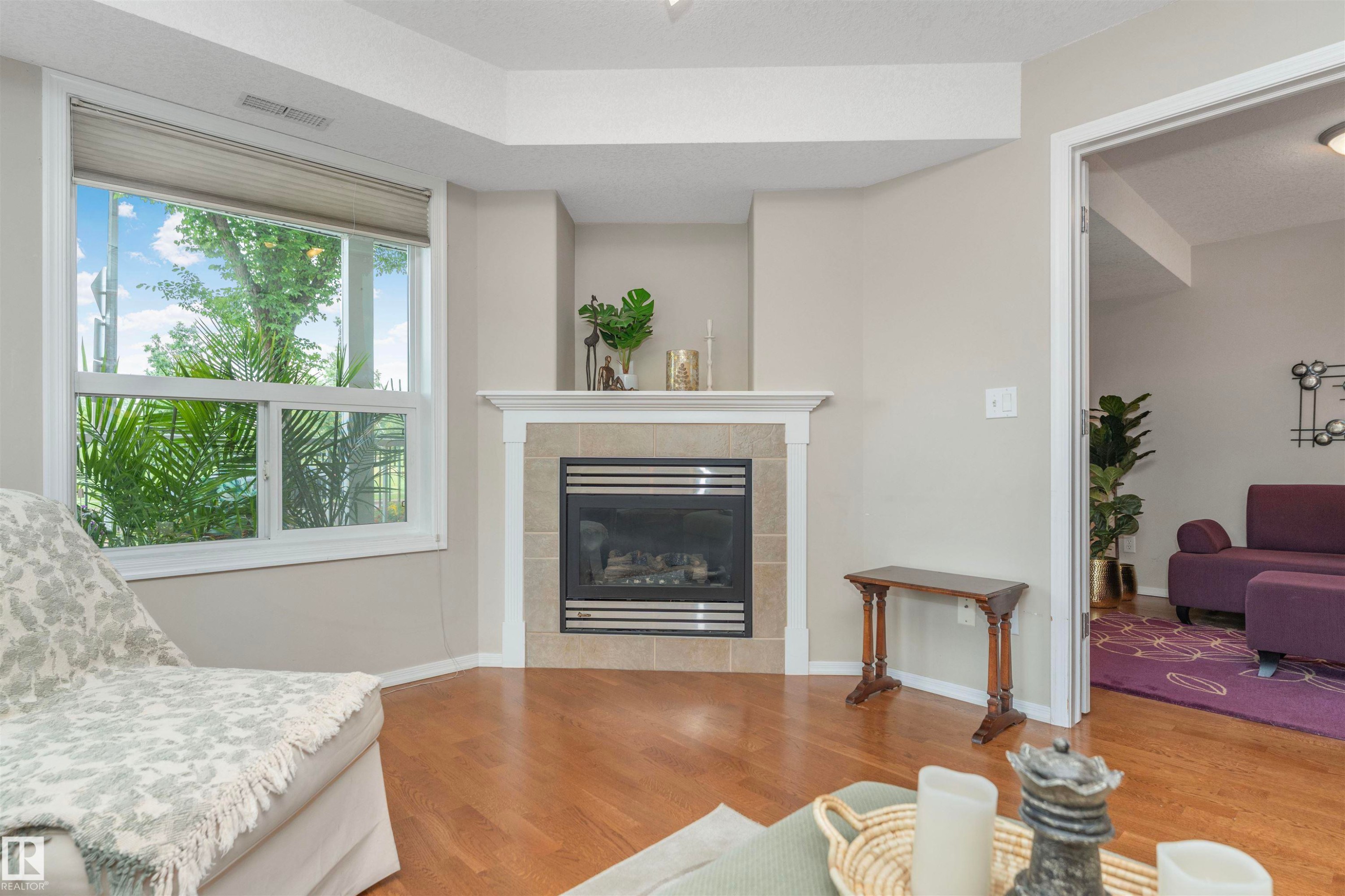 Corner fireplace with a tile surround and white mantel, complemented by wood-finish flooring - #130 9008 99 Av Nw Nw, Edmonton, AB