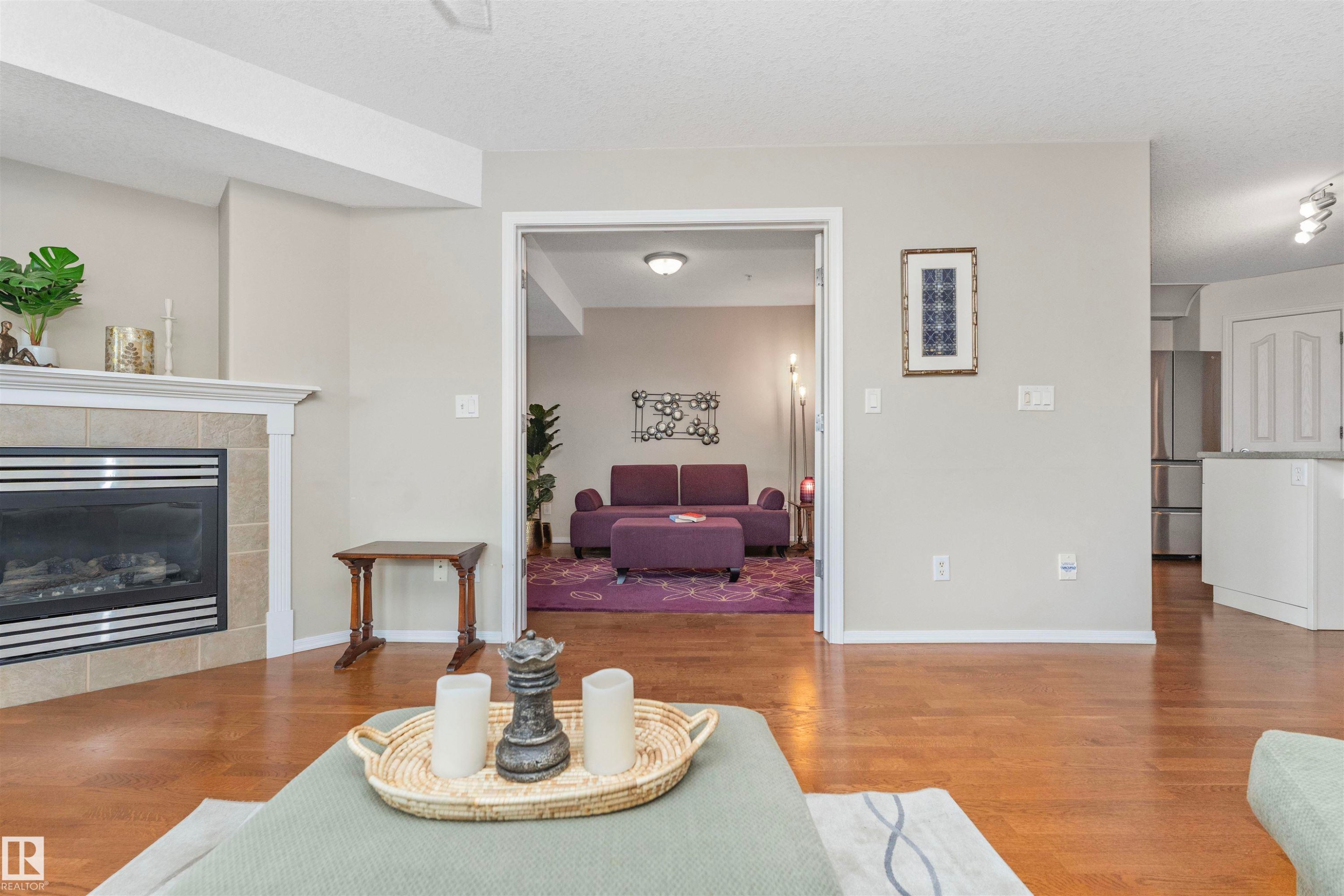 Hardwood-finish flooring throughout, featuring a fireplace with a tiled surround and white mantel - #130 9008 99 Av Nw Nw, Edmonton, AB