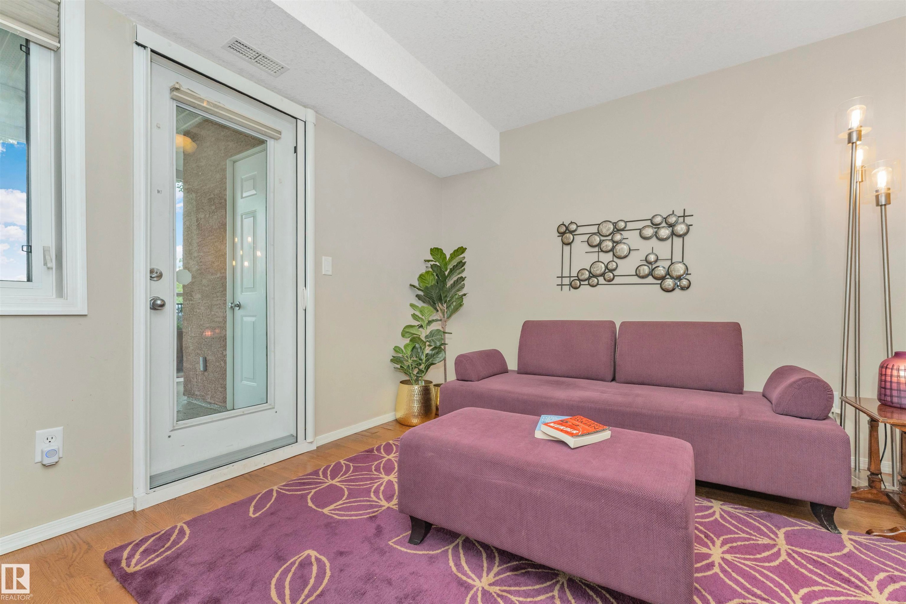 Living space featuring wood-finish flooring, a full-lite glass door, and neutral wall tones - #130 9008 99 Av Nw Nw, Edmonton, AB