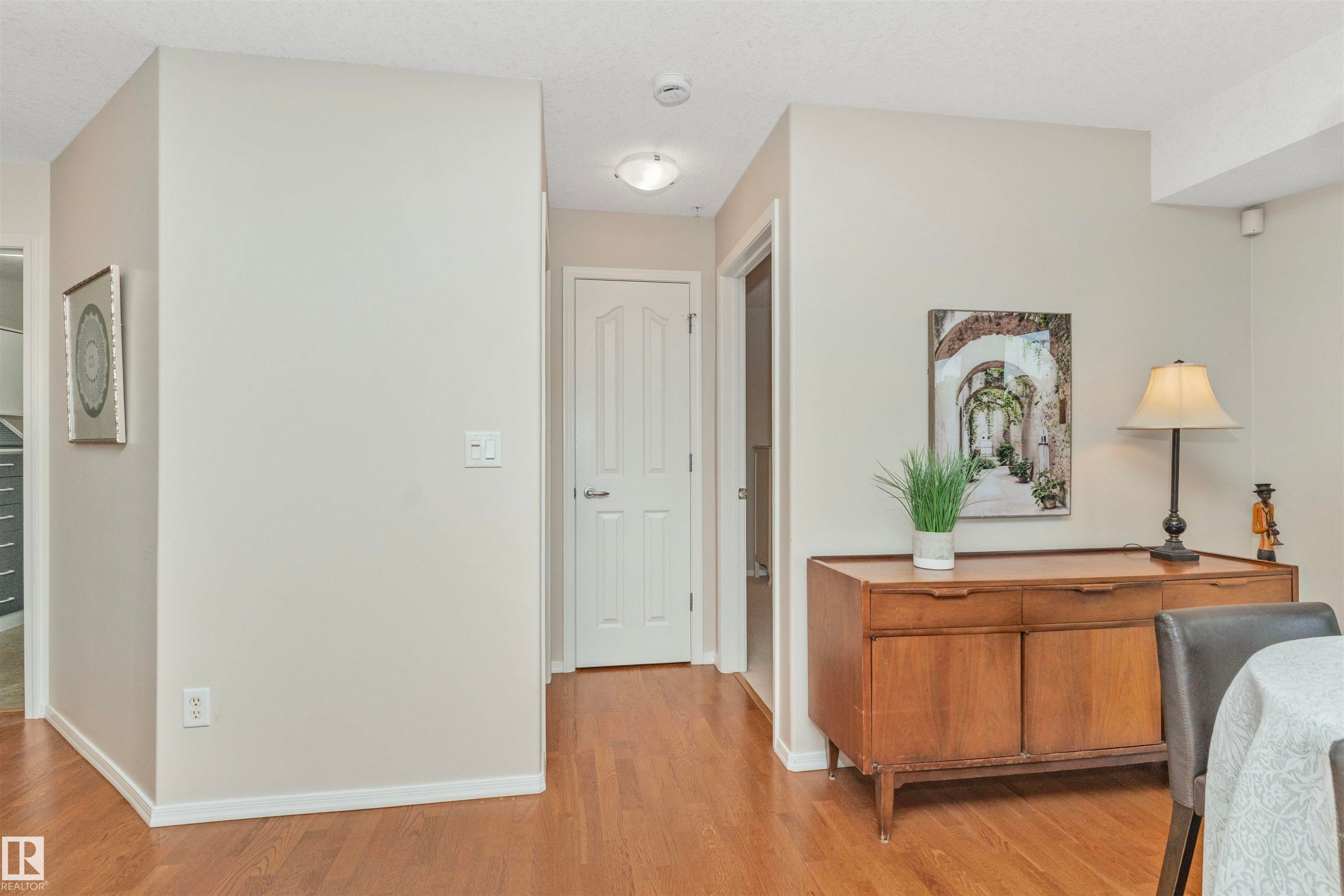 Hardwood flooring throughout a hall area with light-toned walls and white trim - #130 9008 99 Av Nw Nw, Edmonton, AB