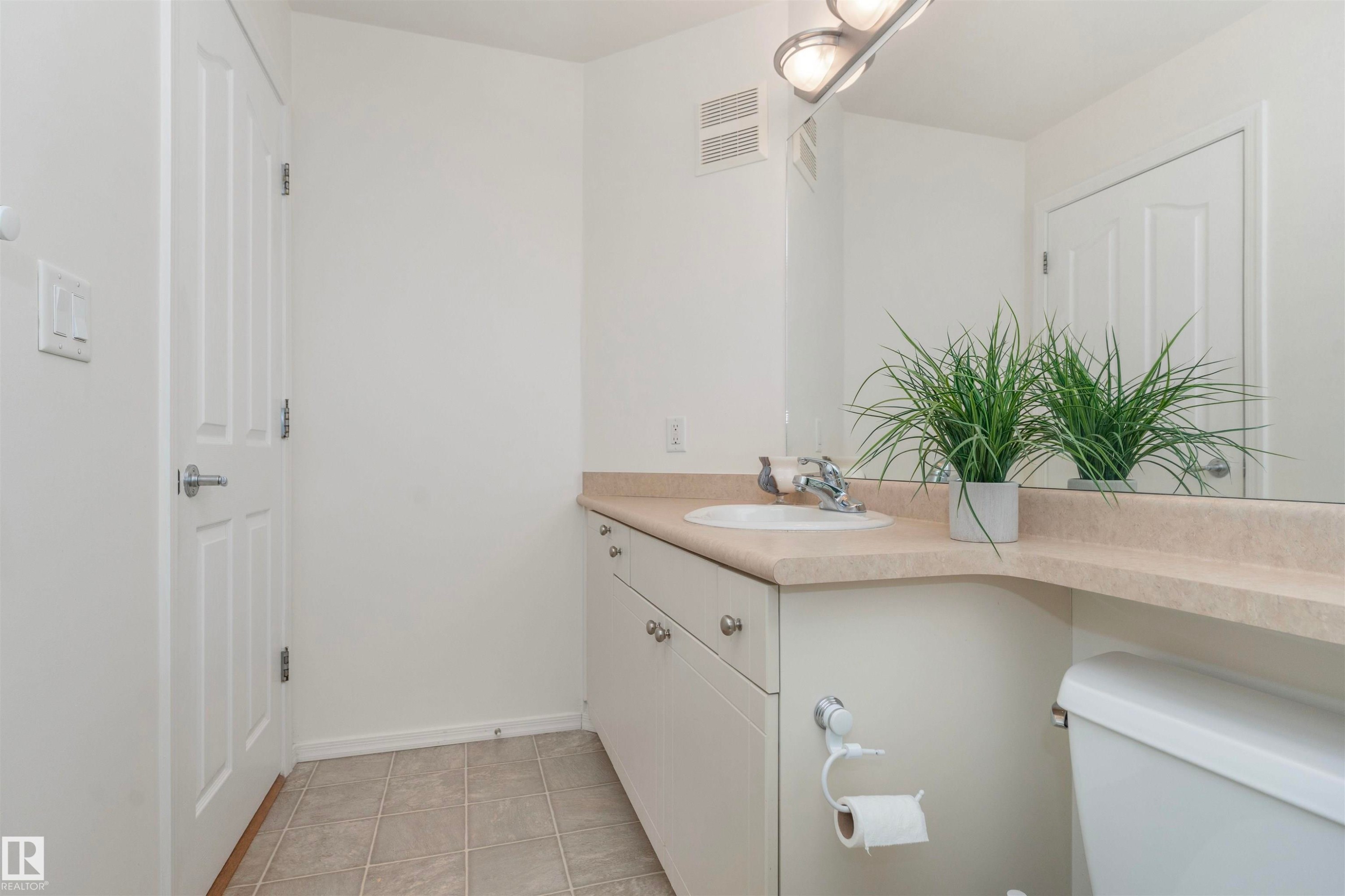 Bathroom vanity featuring an integrated sink, polished chrome faucet, and expansive wall-mounted mirror - #130 9008 99 Av Nw Nw, Edmonton, AB