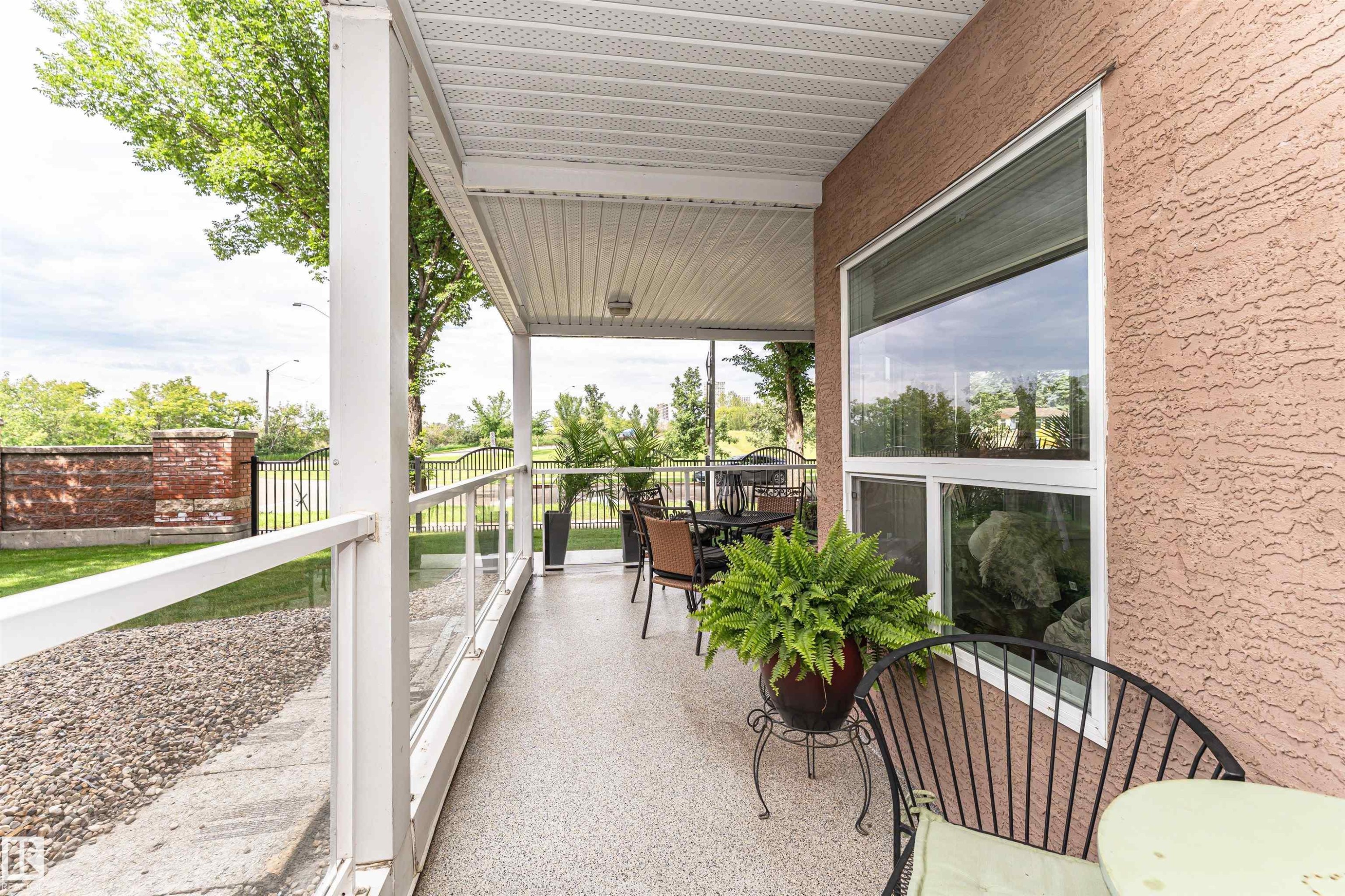 Covered patio featuring a textured exterior, glass railing, and durable composite flooring - #130 9008 99 Av Nw Nw, Edmonton, AB