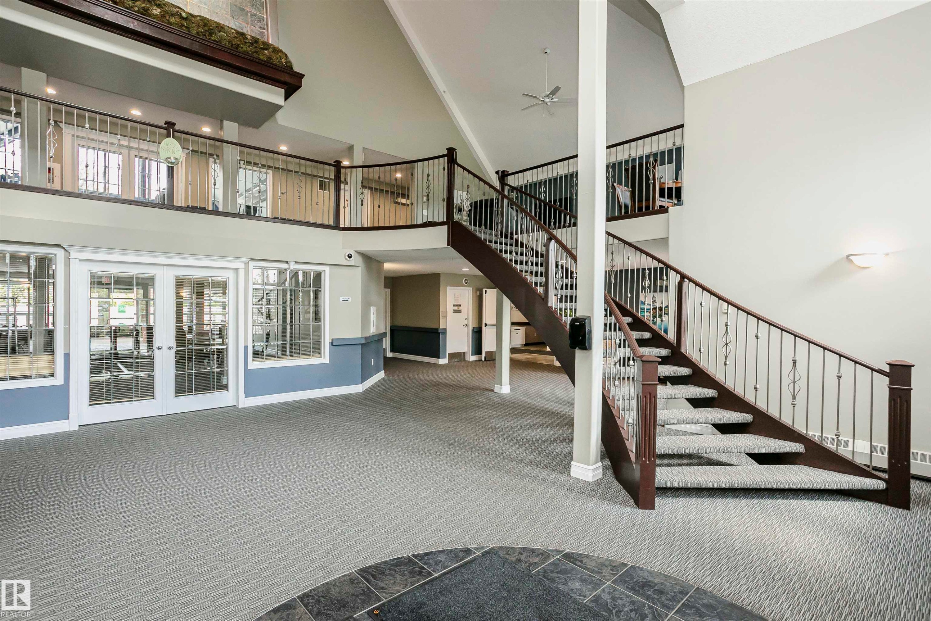 Two-story foyer featuring a grand staircase with dark wood-finish handrails and decorative metal balusters - #130 9008 99 Av Nw Nw, Edmonton, AB