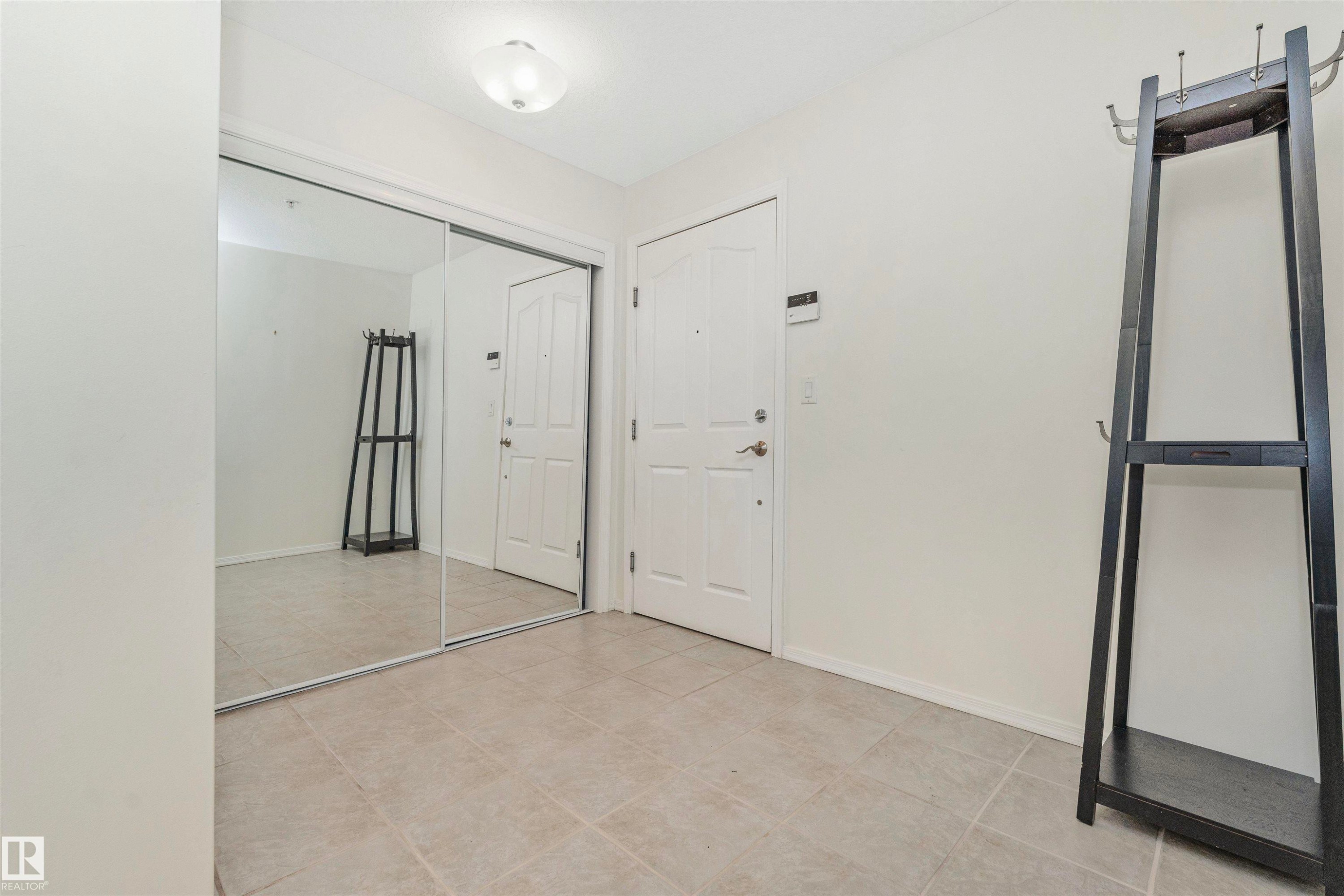 Entryway featuring light-toned tile flooring and a full-height mirrored closet - #130 9008 99 Av Nw Nw, Edmonton, AB