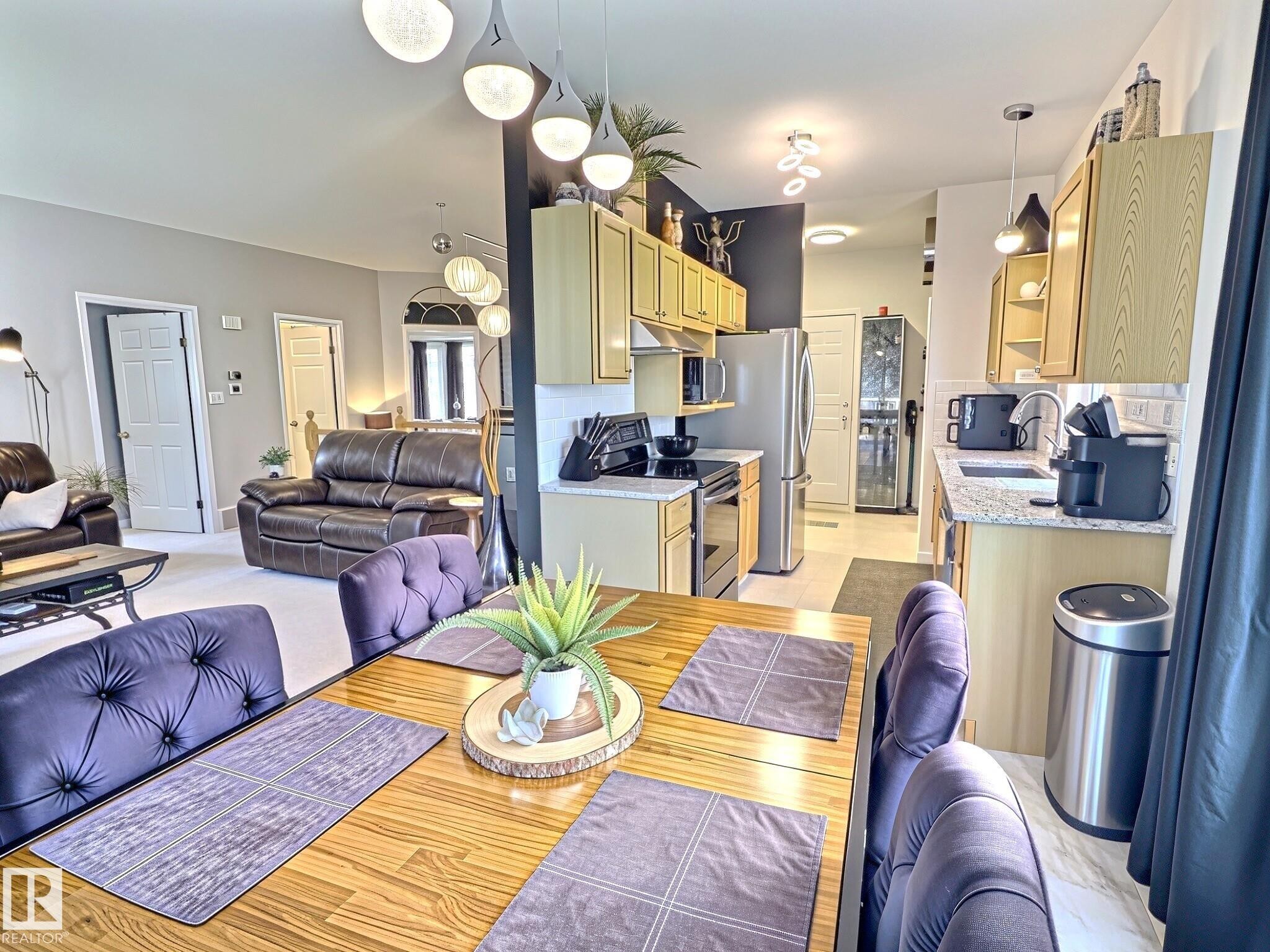 Open concept living space featuring a dining area with wood-finish flooring, a kitchen with light wood-finish cabinetry, stainless steel appliances, and a tiled backsplash, and a living area with light-colored carpeting - 17 10 Blackburn Drive, Edmonton, AB