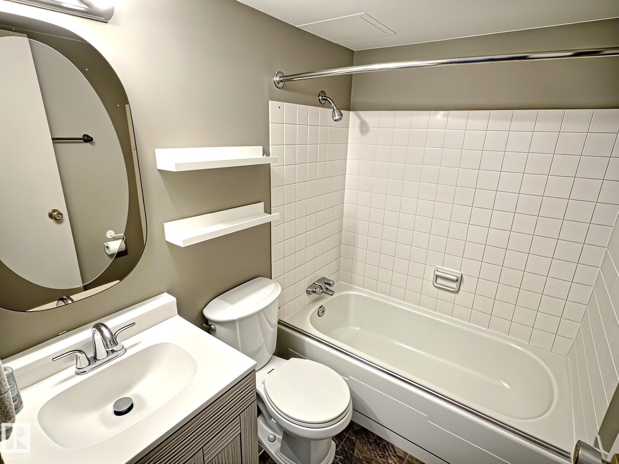 Full bathroom featuring a white vanity with integrated sink, chrome faucet, oval mirror, and a full-size bathtub with white subway tile surround - 1105 11007 83 Avenue, Edmonton, AB