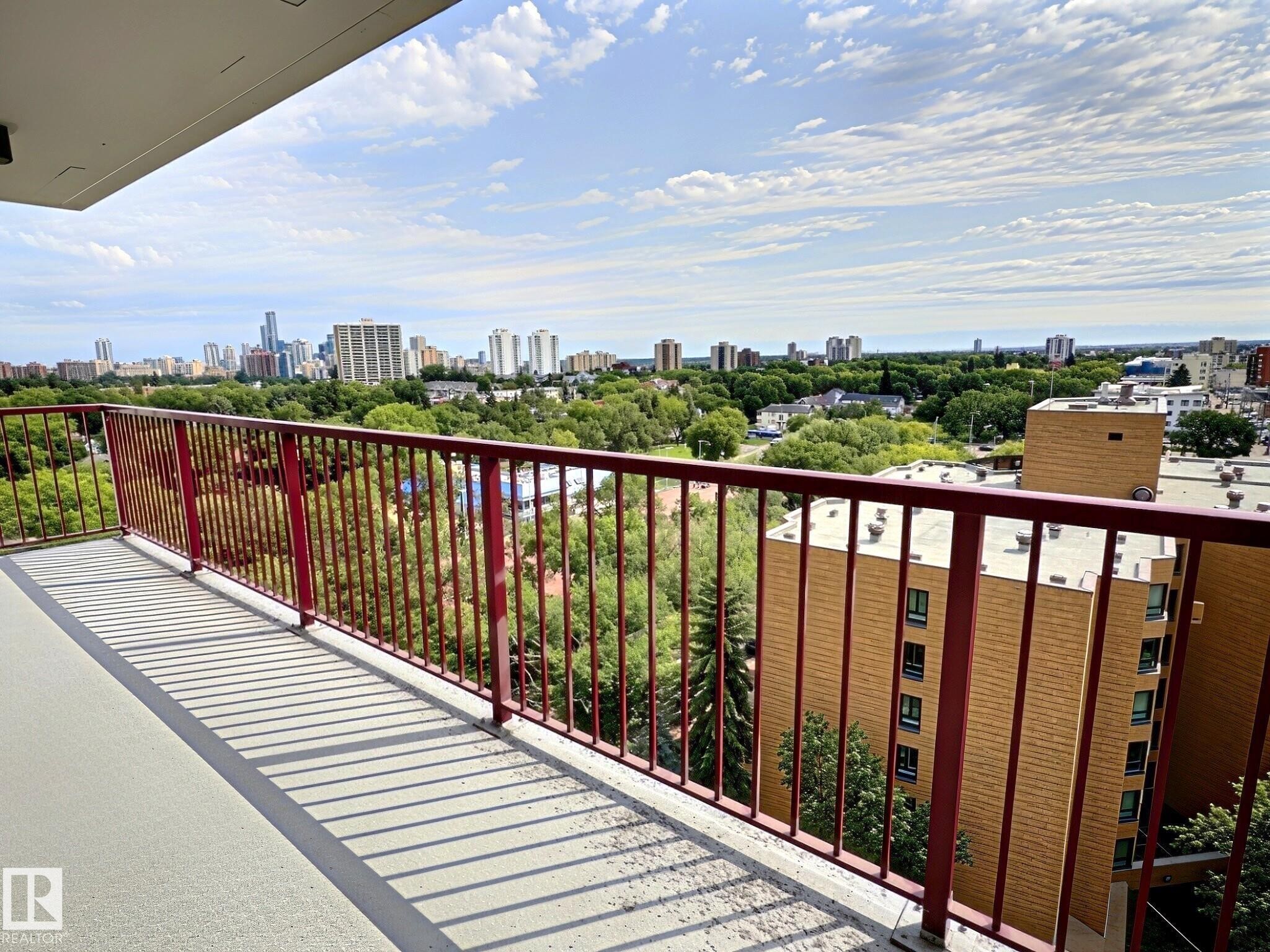 Private balcony featuring a red metal railing, concrete flooring, and an urban skyline backdrop - 1105 11007 83 Avenue, Edmonton, AB