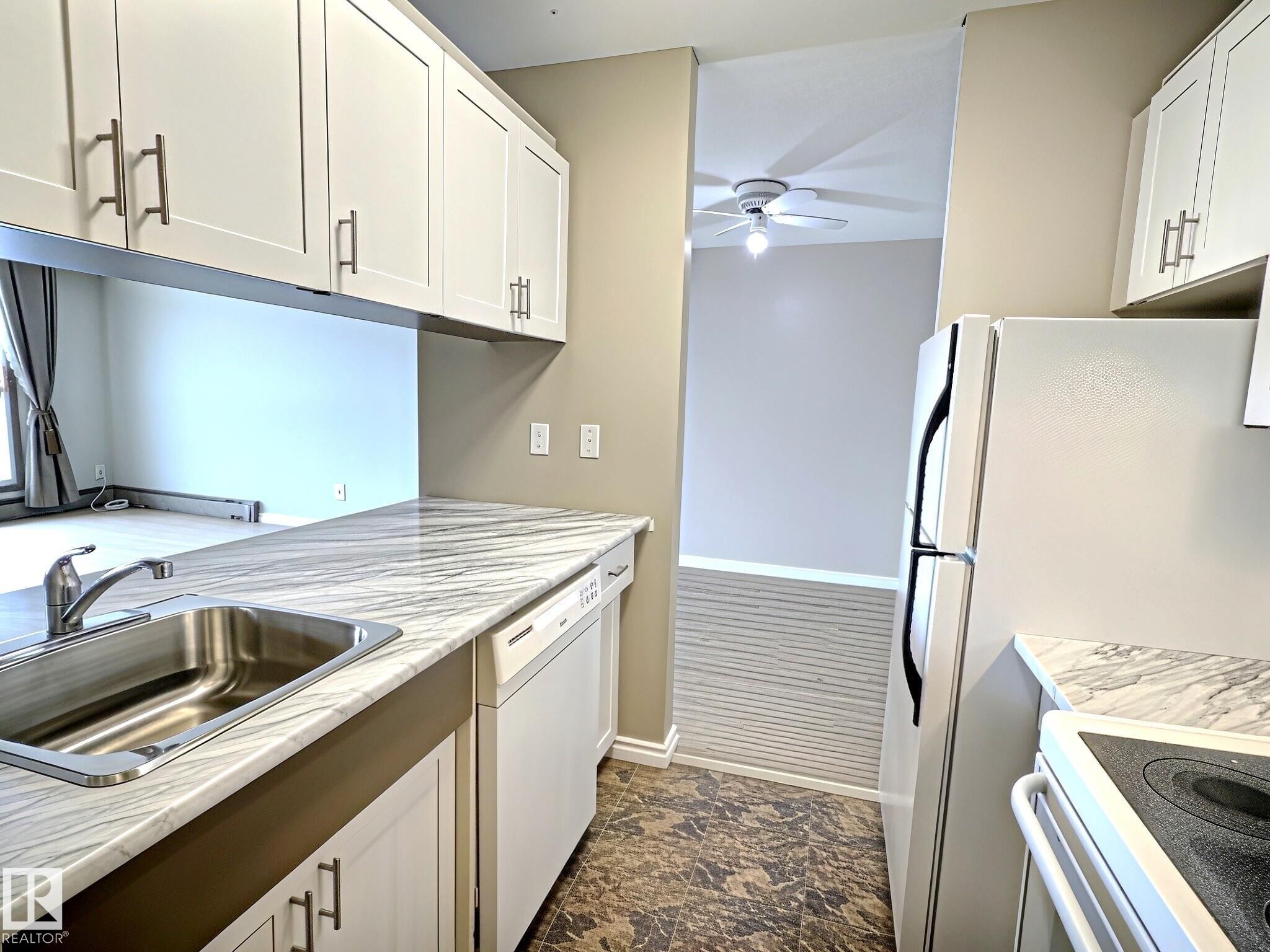 Kitchen featuring white shaker-style cabinetry with brushed nickel hardware, a stainless steel sink, and white-marbled countertops - 1105 11007 83 Avenue, Edmonton, AB