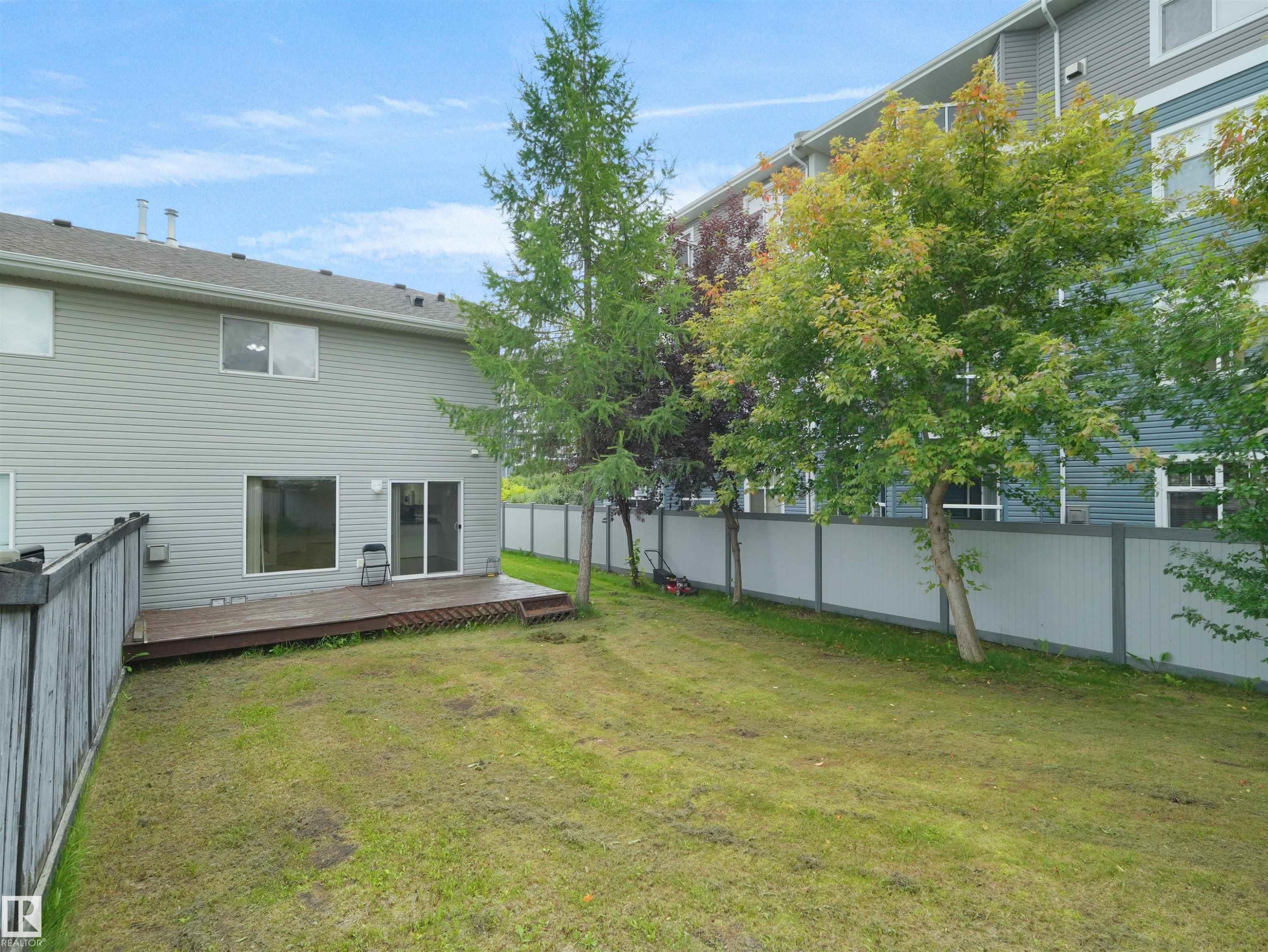 Expansive grassed area featuring a wooden deck with railing and direct access to the interior via a sliding glass door - 16106 131A Street Nw, Edmonton, AB - Outdoor