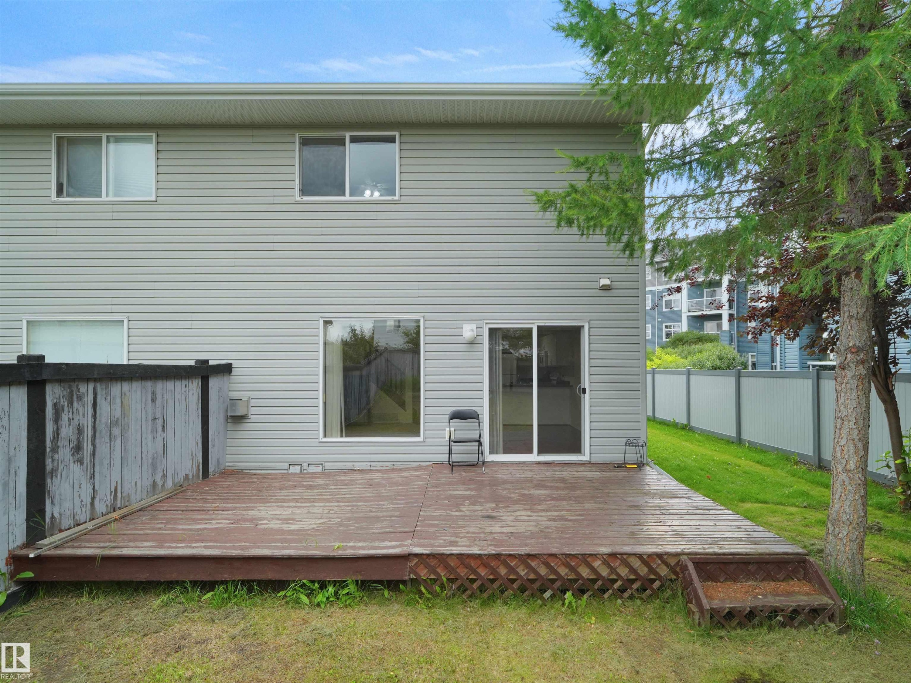 Rear exterior featuring a ground-level wood-finish deck with lattice trim, sliding glass door access, and light grey horizontal siding - 16106 131A Street Nw, Edmonton, AB - Outdoor With Exterior