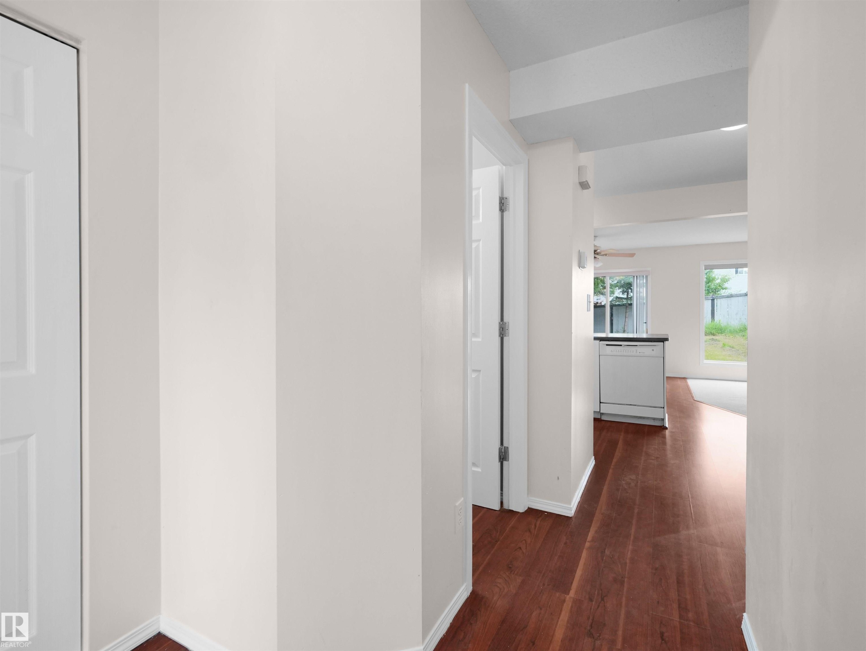 Hallway featuring rich wood-finish flooring, white baseboards, and a doorway leading to an interior space with a built-in dishwasher - 16106 131A Street Nw, Edmonton, AB - Indoor Photo Showing Other Room