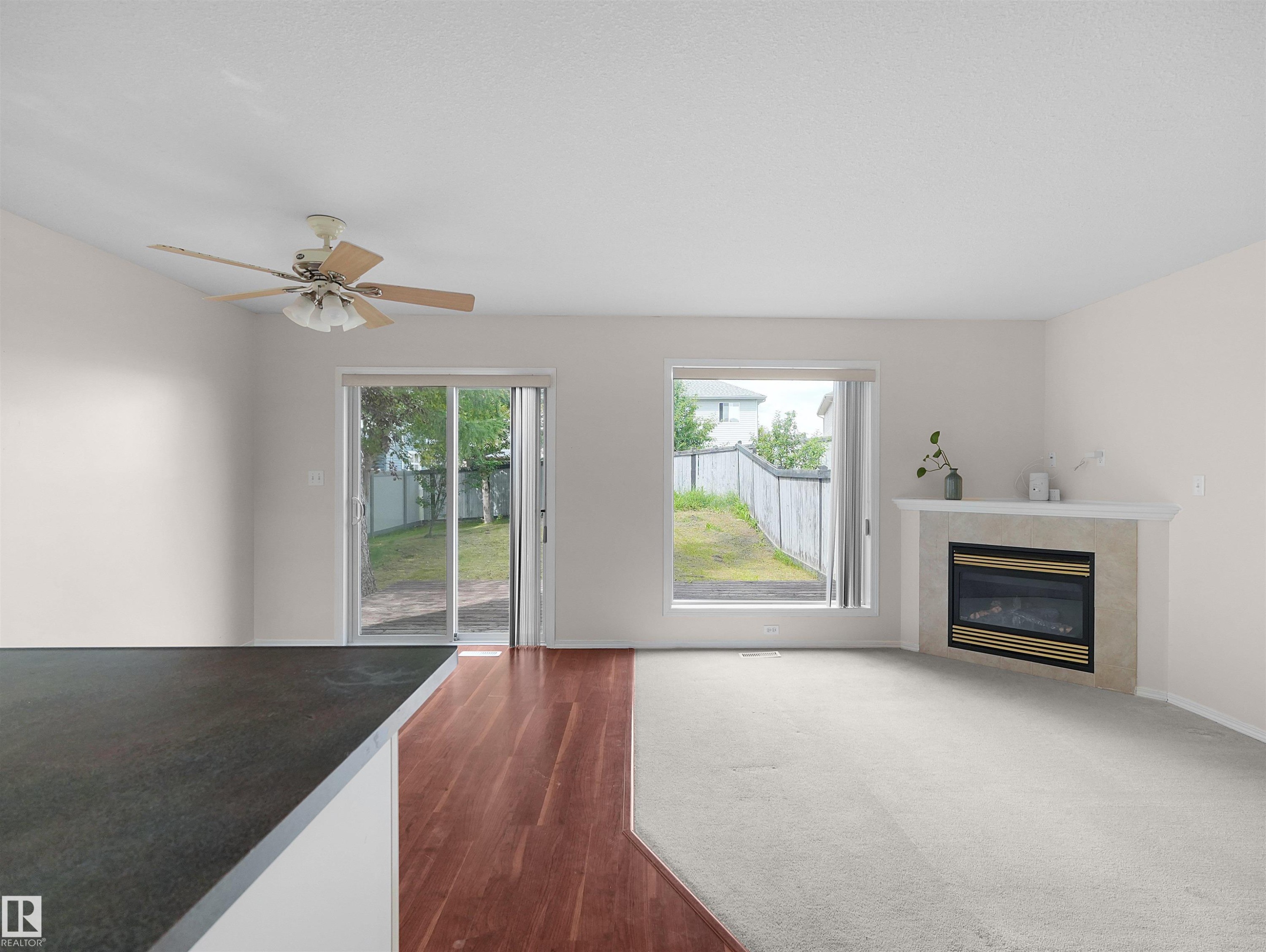 Living area featuring a gas fireplace with a tiled surround, a large window, and sliding glass doors leading to the exterior - 16106 131A Street Nw, Edmonton, AB - Indoor Photo Showing Living Room With Fireplace