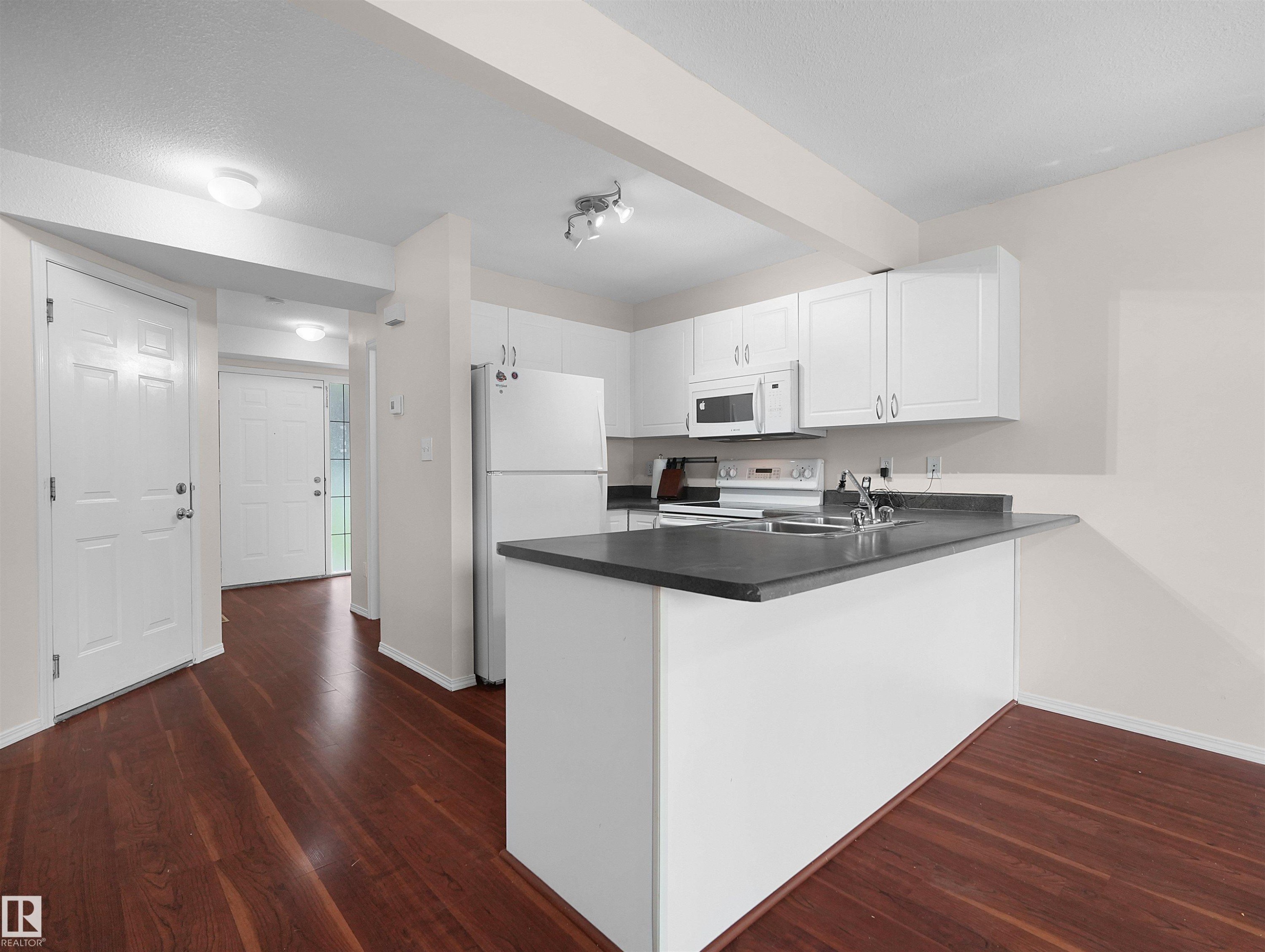 Open-concept kitchen featuring white cabinetry, dark countertops, and integrated appliances - 16106 131A Street Nw, Edmonton, AB - Indoor Photo Showing Kitchen