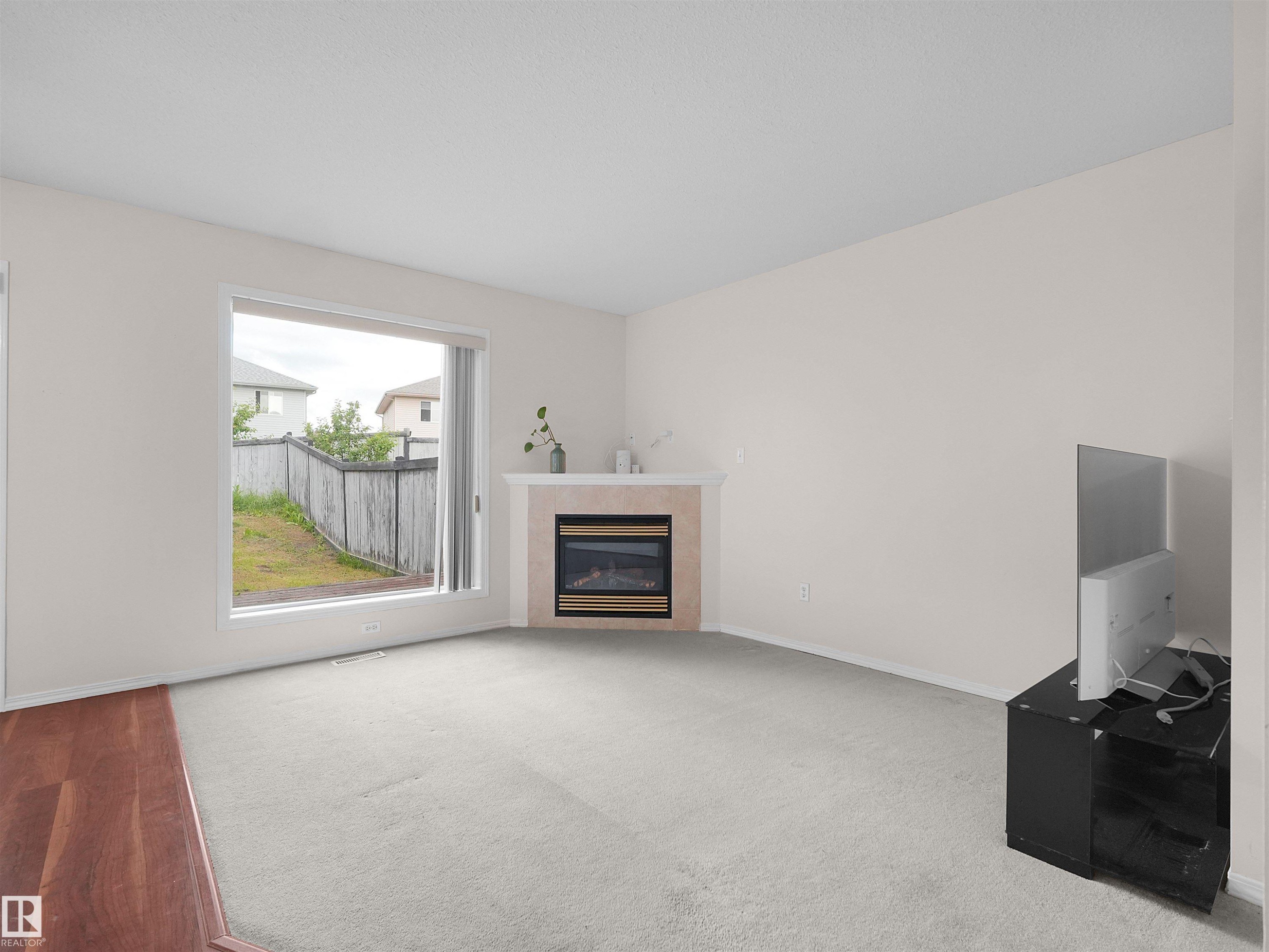 Living room with a large window, light-colored walls, and carpeting - 16106 131A Street Nw, Edmonton, AB - Indoor Photo Showing Living Room With Fireplace