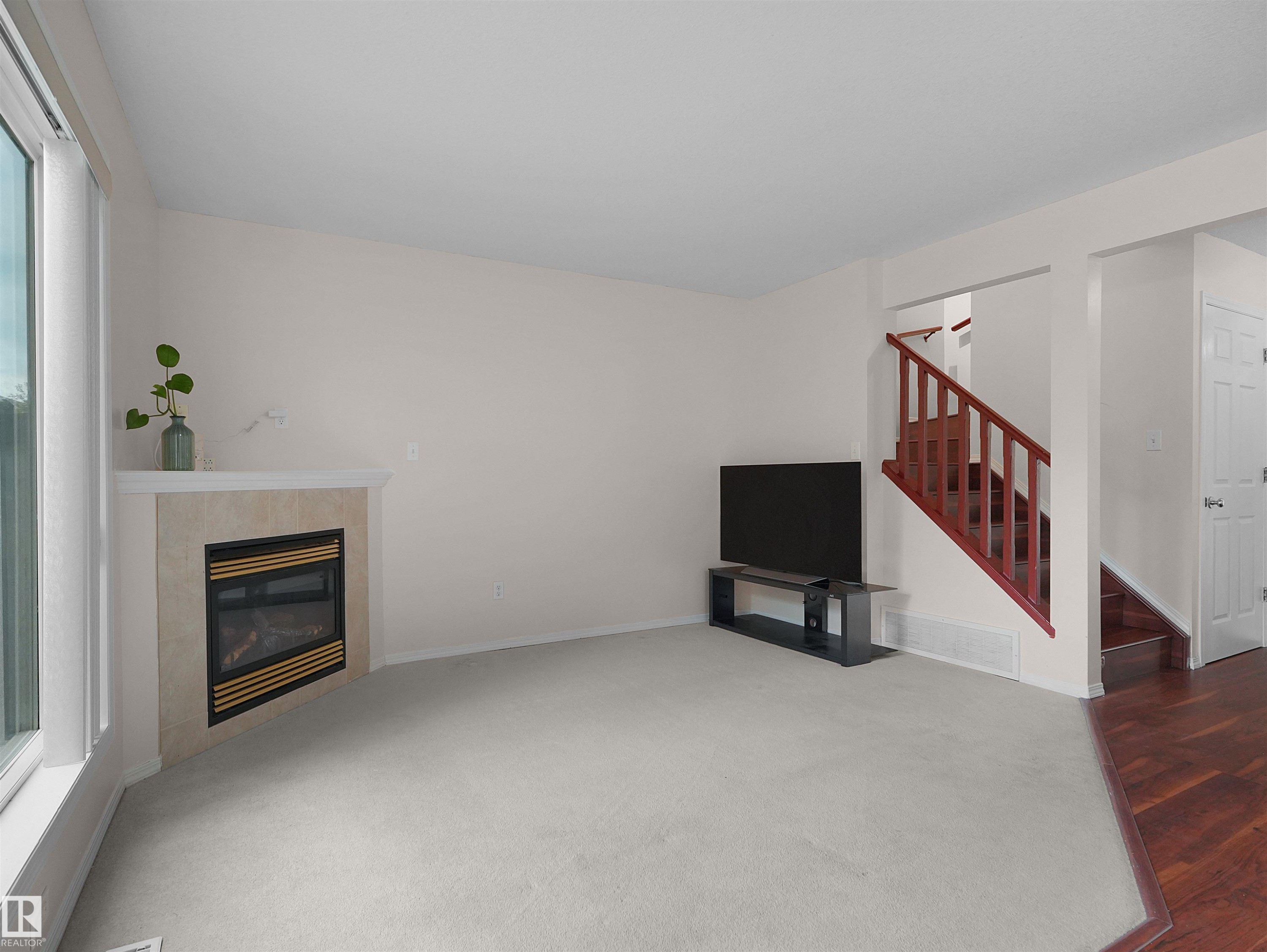 Living area featuring a corner fireplace with a tiled surround, light carpet flooring, and a large window - 16106 131A Street Nw, Edmonton, AB - Indoor Photo Showing Other Room With Fireplace