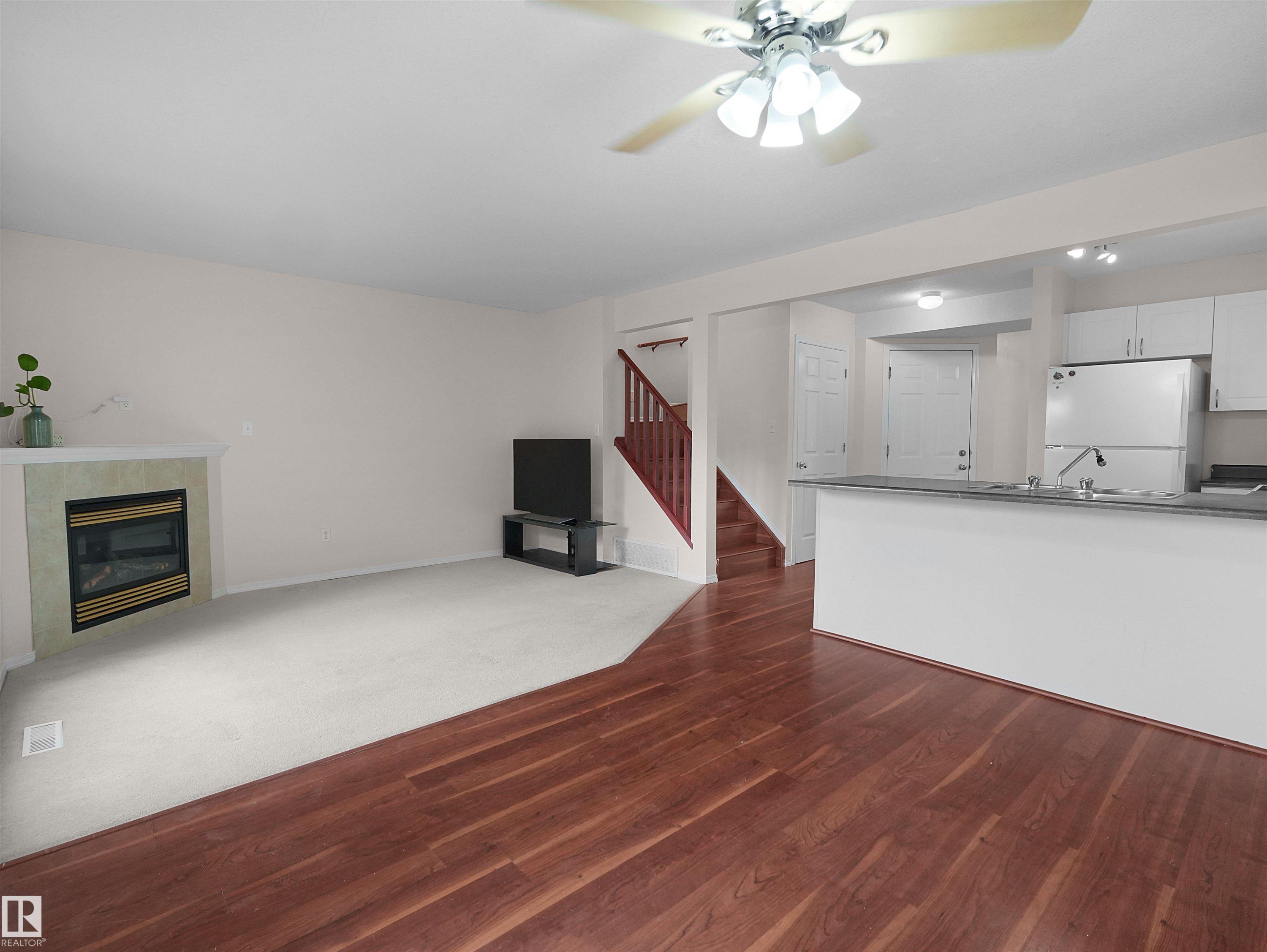 Open-concept living area featuring a fireplace with a tile surround and white mantel, wood-finish flooring, and a ceiling fan with integrated lighting - 16106 131A Street Nw, Edmonton, AB - Indoor With Fireplace