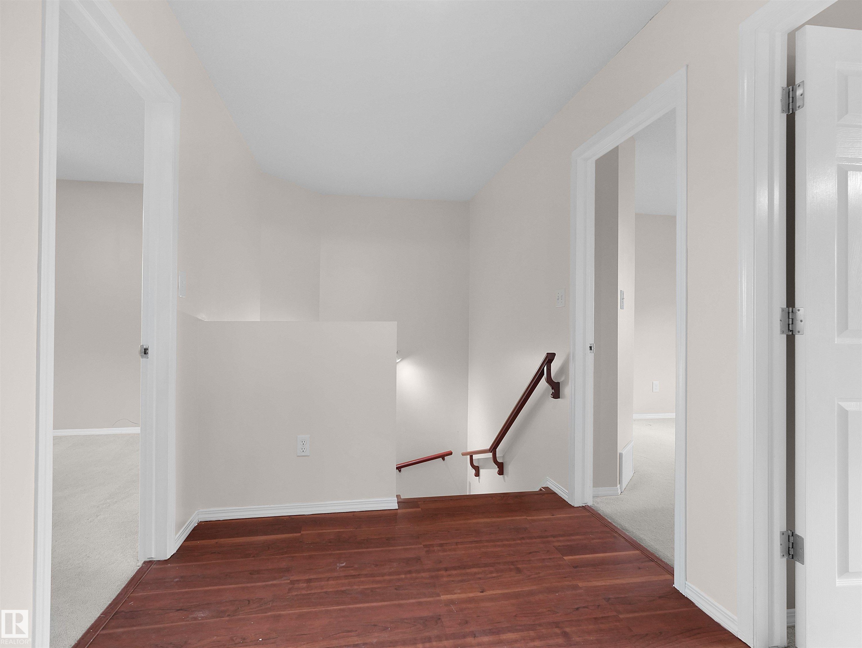 Upper-level landing featuring wood-finish flooring, light-toned wall paint, white trim, and a wood handrail leading downstairs - 16106 131A Street Nw, Edmonton, AB - Indoor Photo Showing Other Room