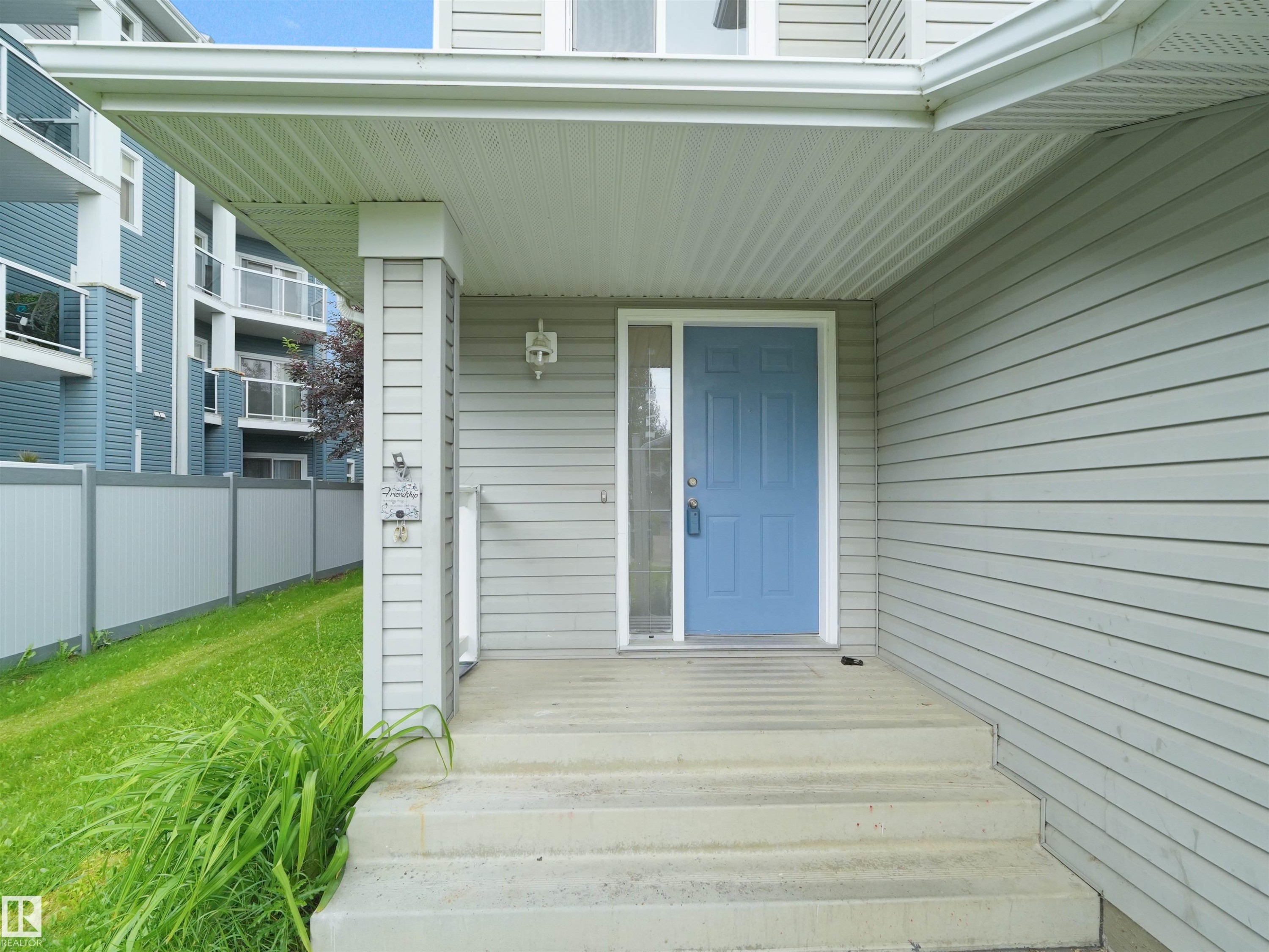Covered entryway featuring a blue front door with a sidelight, concrete steps, and light gray horizontal siding - 16106 131A Street Nw, Edmonton, AB - Outdoor With Exterior