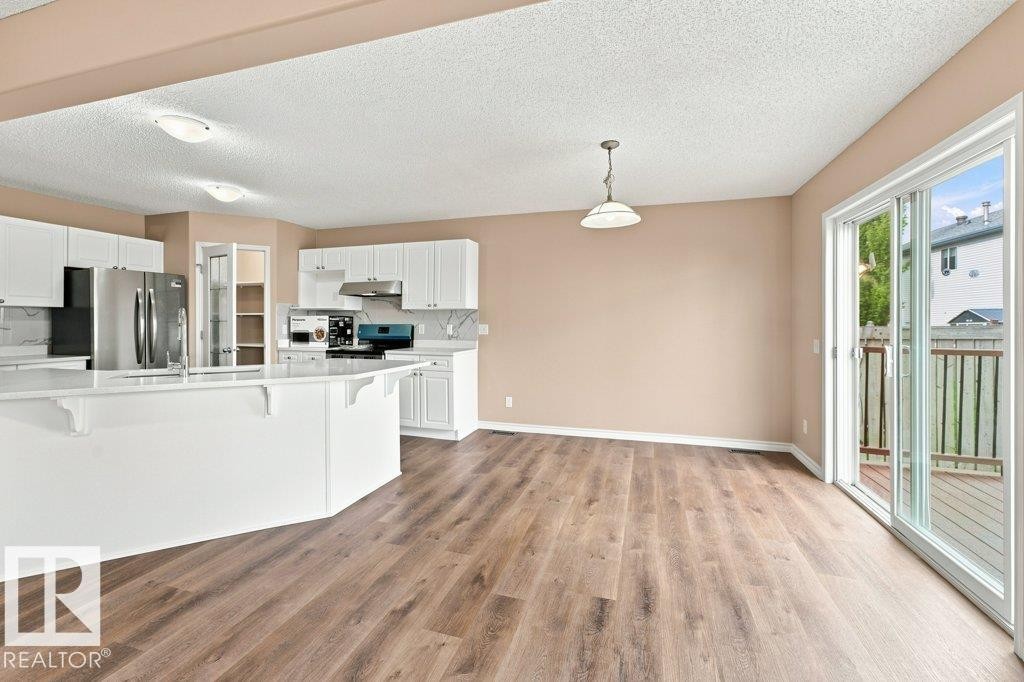 Open-concept living space featuring wood-finish flooring, a kitchen island with white cabinetry and light countertops, stainless steel appliances, and sliding glass doors opening to an outdoor deck - 2811 33 Street, Edmonton, AB