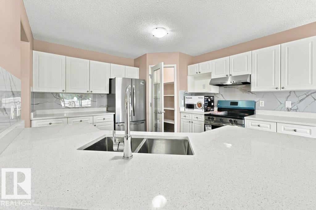 Kitchen featuring white cabinetry, light-toned countertops, a stainless steel sink, and a matching appliance suite - 2811 33 Street, Edmonton, AB