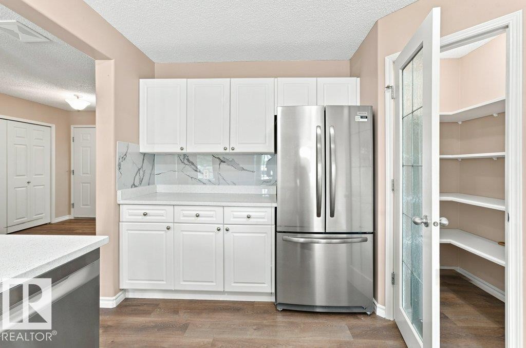 Kitchen featuring white shaker-style cabinetry, a stainless steel French door refrigerator, and wood-finish flooring - 2811 33 Street, Edmonton, AB