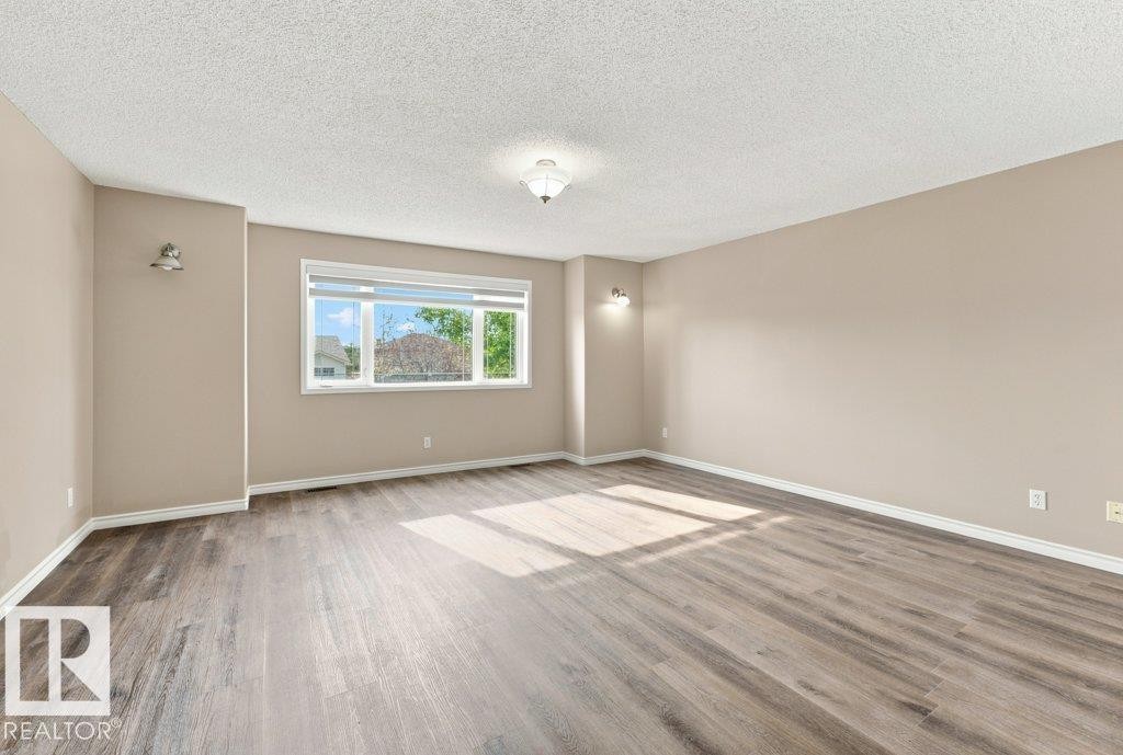 Spacious room featuring wood-finish flooring, neutral-toned walls, and a large window with white blinds - 2811 33 Street, Edmonton, AB