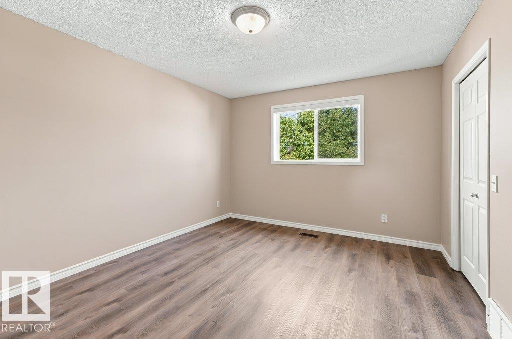 Room featuring wood-finish flooring, a window with natural light, and a white paneled door - 2811 33 Street, Edmonton, AB