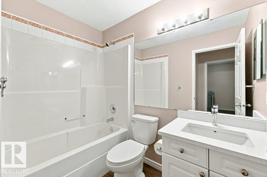 Bathroom featuring a white bathtub and shower surround with decorative tile accent, a vanity with a white countertop and integrated sink, a large mirror, and a modern light fixture - 2811 33 Street, Edmonton, AB