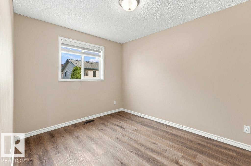 Room featuring a window with white blinds, neutral wall paint, and wood-finish flooring - 2811 33 Street, Edmonton, AB