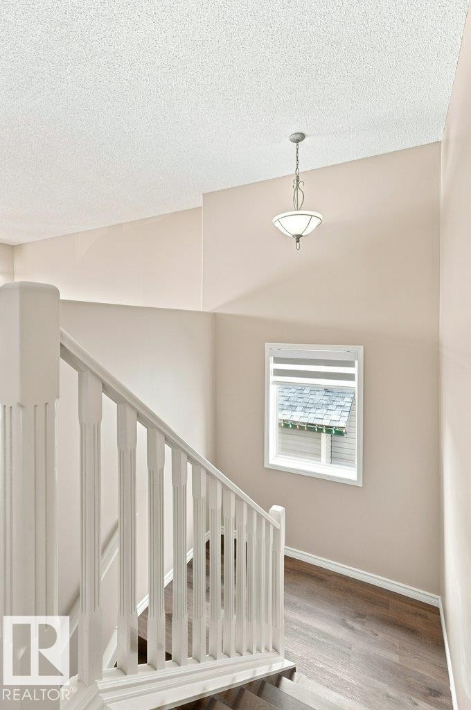 Staircase featuring white balusters and newel posts, wood-finish flooring, a window with horizontal blinds, and a suspended ceiling light fixture - 2811 33 Street, Edmonton, AB